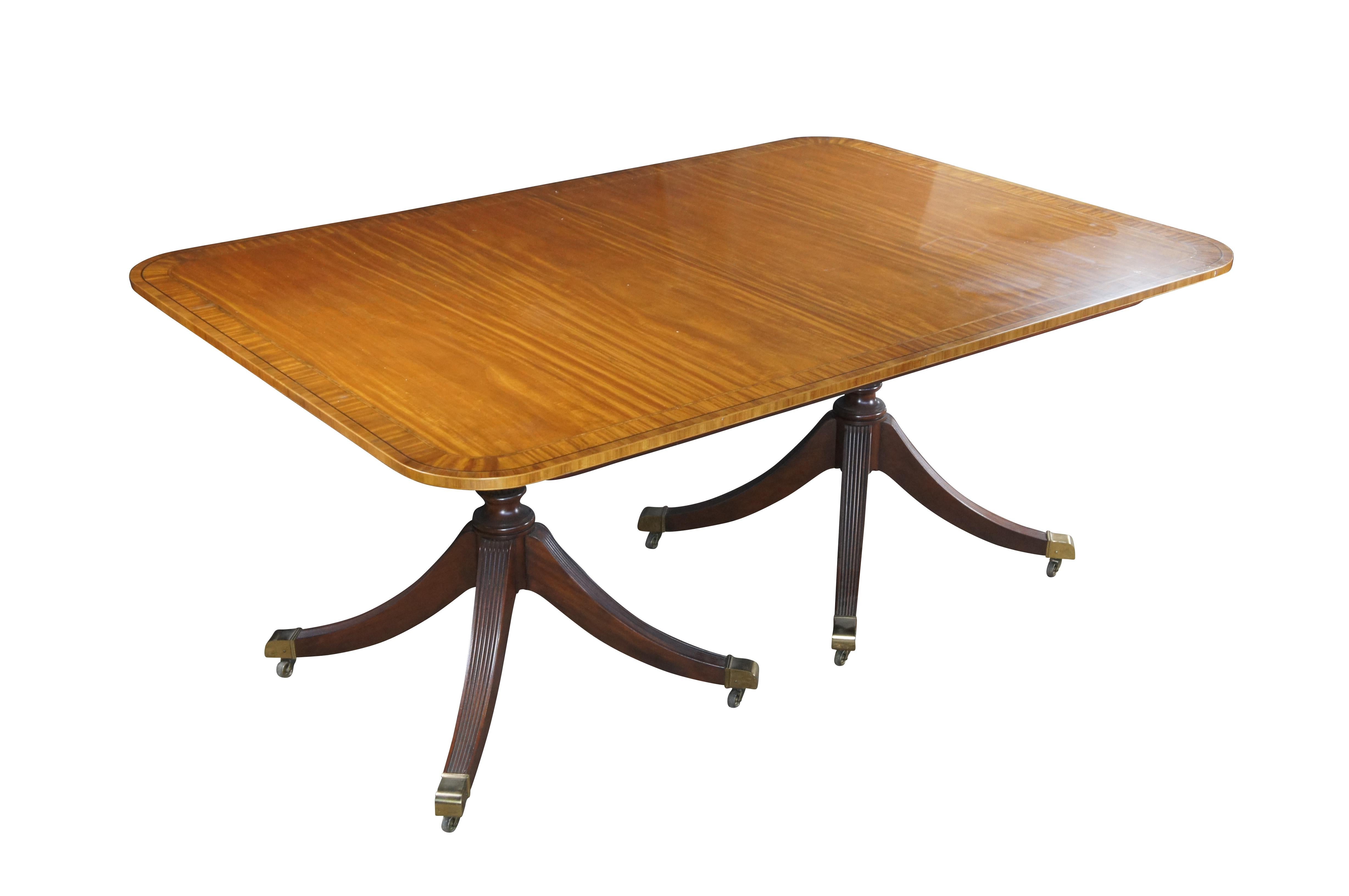 Baker Furniture Collectors Edition English Regency Duncan Phyfe dining table. Features an impressive satinwood cross banded and inlaid top.  The table is supported by a double pedestal mahogany base with shapely reeded urns over four downswept
