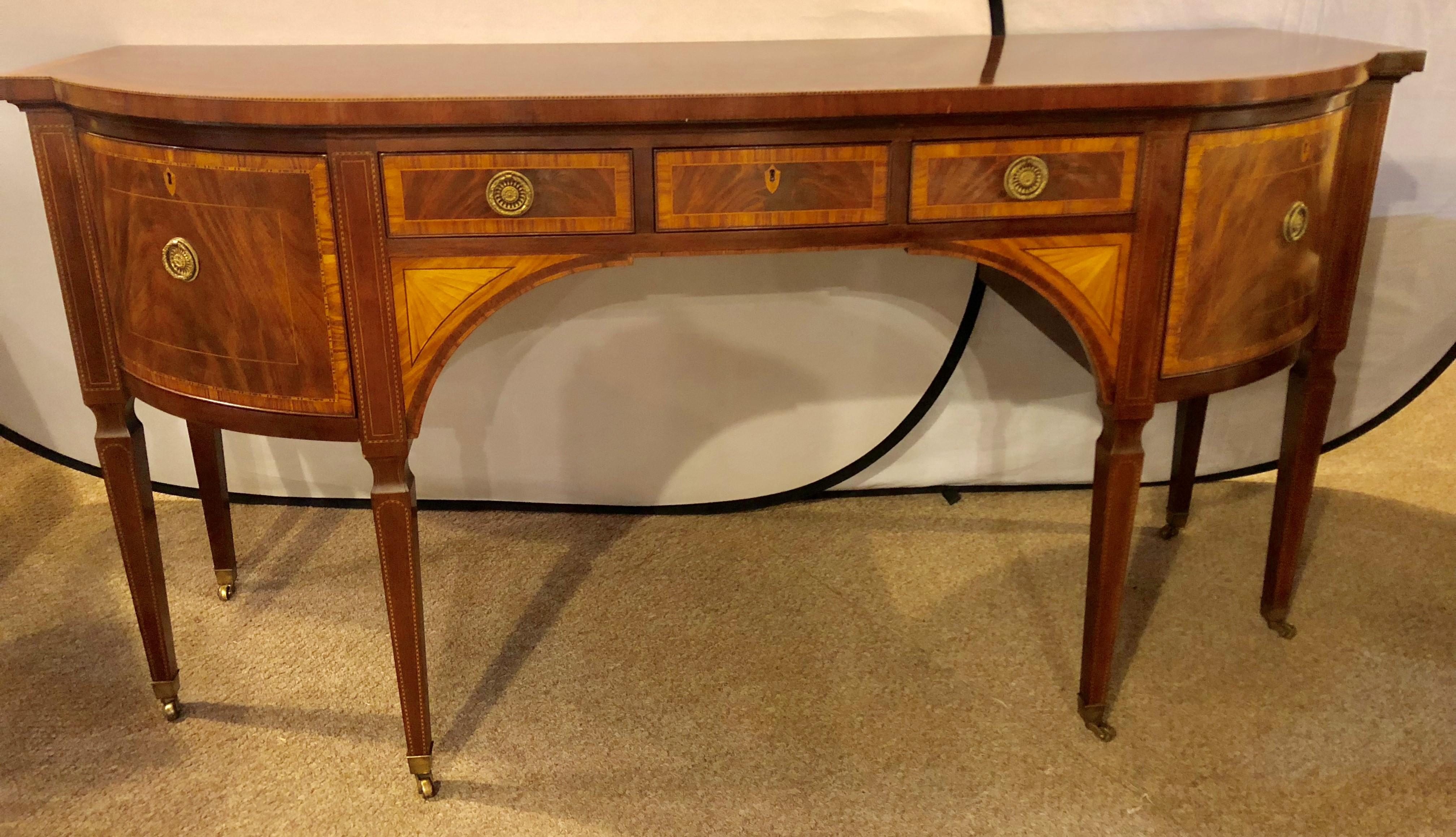 A Baker Fine Furniture Company Stately Homes Sheraton style mahogany and satinwood inlaid sideboard. The bronze casters leading to tapering legs of solid mahogany supporting an upper shell of two satinwood banded crotch mahogany doors flanking a