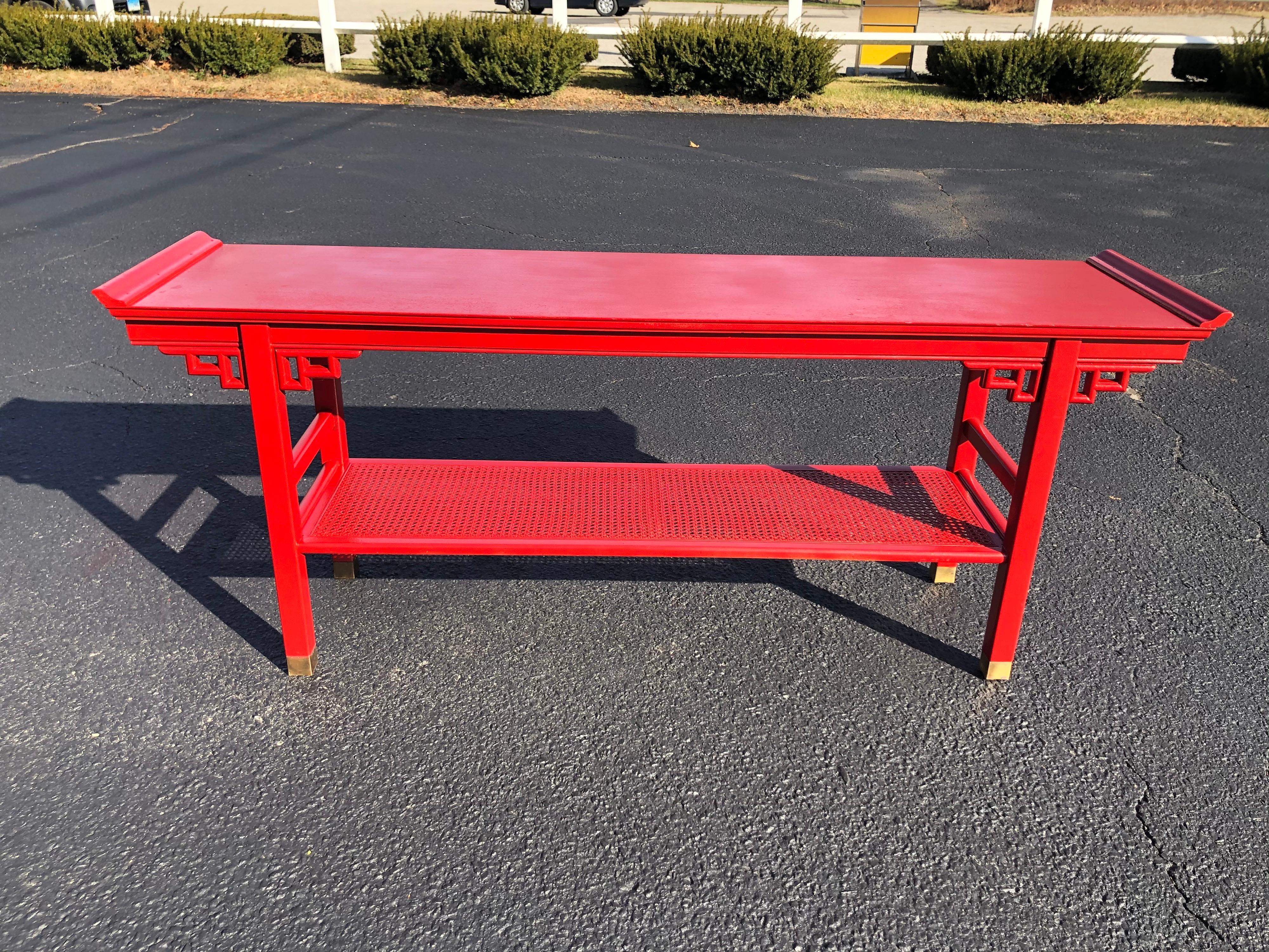 Baker style Asian two tiered console table in Red. Perfect way to brighten up your entry way or behind a sofa.
Beautiful fretwork with nice detail. Caning on the lower shelf and nice capped brass feet. Distance between shelves is 14