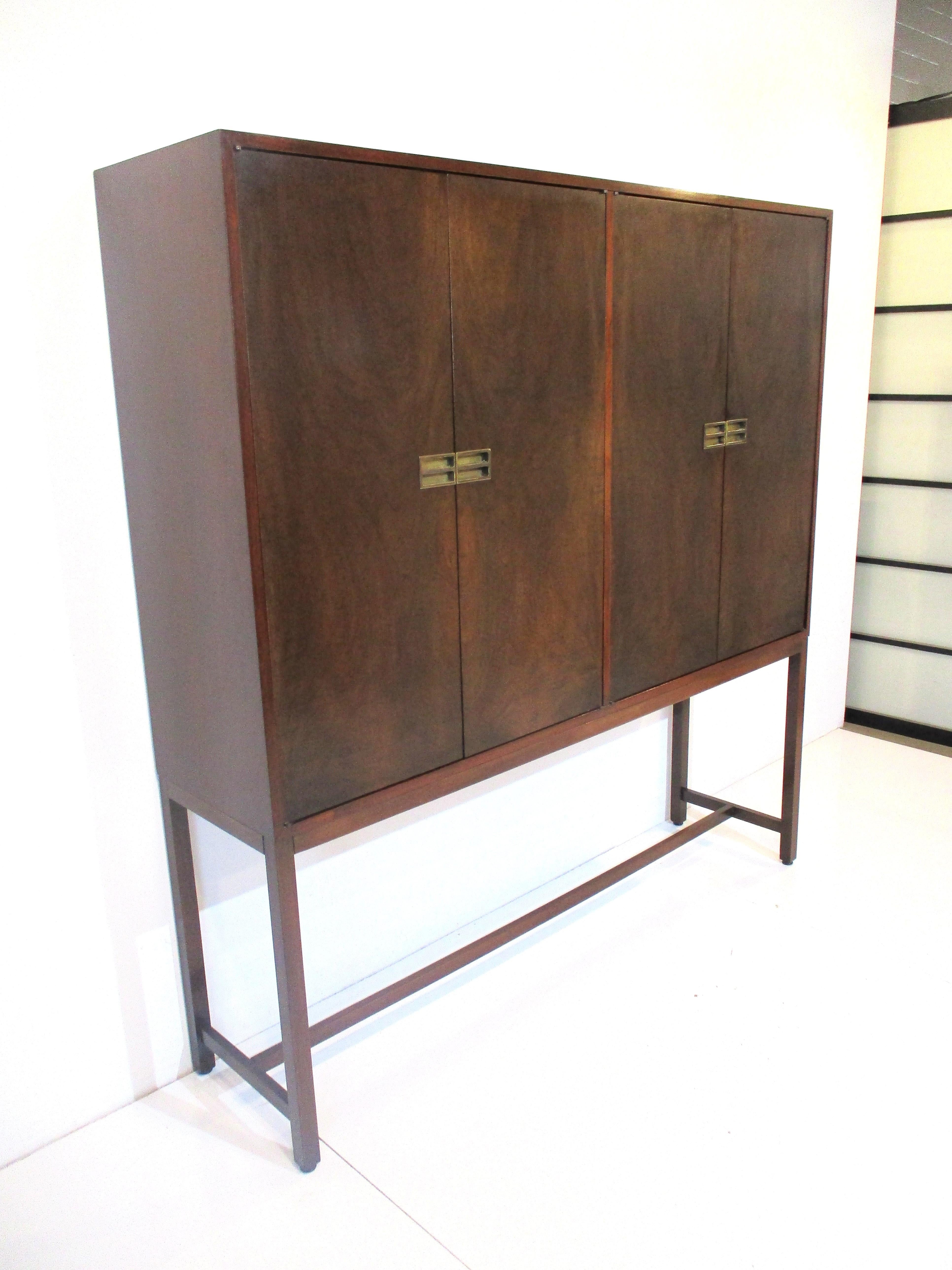 A very well crafted two piece four door cabinet with book matched wood grained fronts opening to revel two glass and two wooden adjustable shelves with two smaller drawers one with dividers. The doors have brass pulls that have a nice textured look