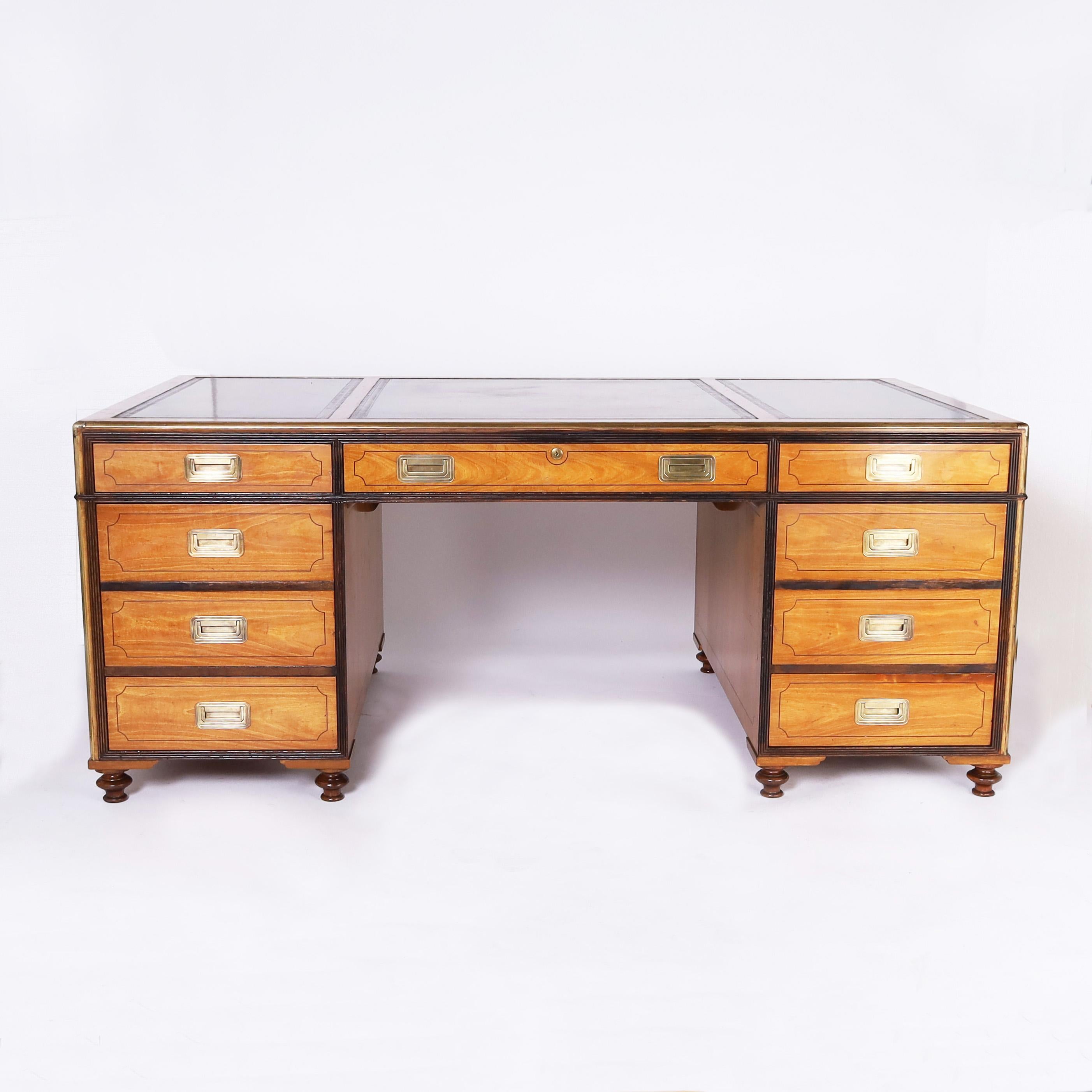 Handsome Mid Century partners desk crafted in mahogany with ebony trim and brass hardware featuring three tooled leather panels on the top over a campaign style twin pedestal form having ten drawers on one side and three drawers and two cabinets on