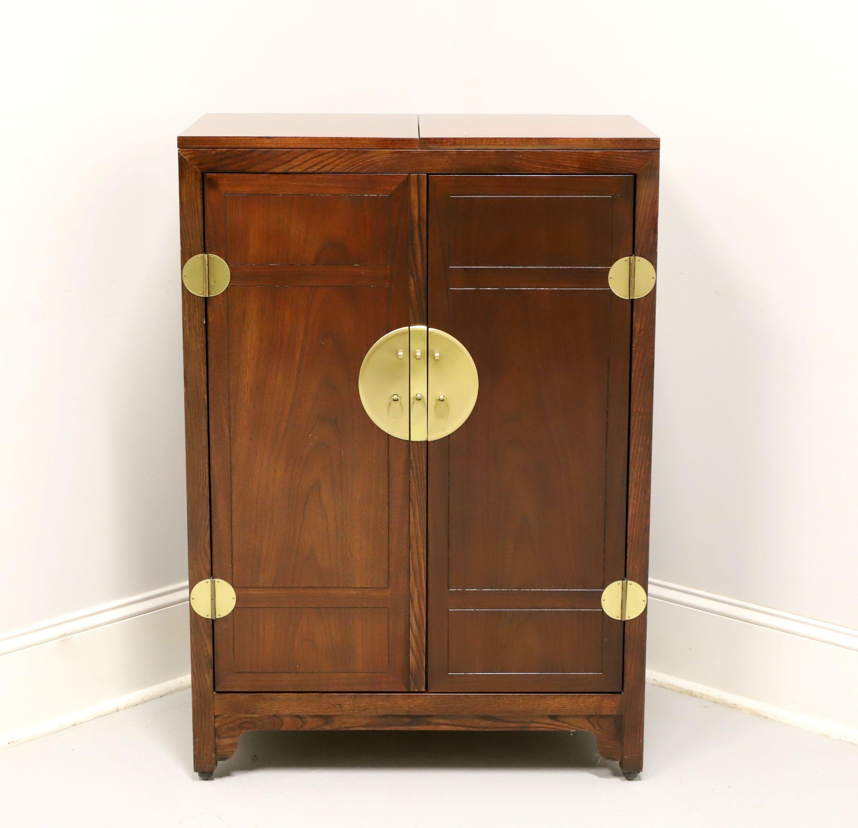 An Asian inspired bar cabinet by Baker Furniture. Walnut, laminate surface under the flip out top, pull out wood supports for flip out top, decorative brass hardware & accents, and bracket feet with casters. Features two doors revealing one upper