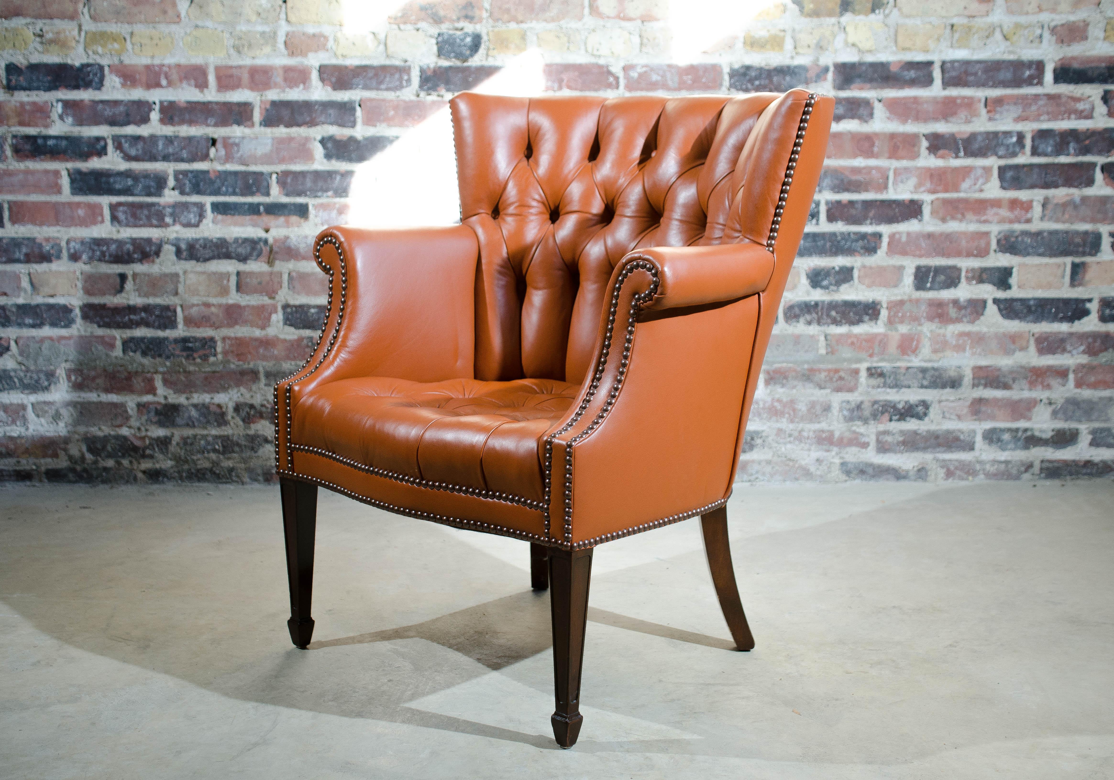 A fully restored, perfectly sized, 1930s tufted Baker wing back chair. Beautiful smaller scale chair, reupholstered with a soft and supple Holly Hunt high quality leather.  The leather is a luscious warm spice color. Legs are stained dark walnut. It