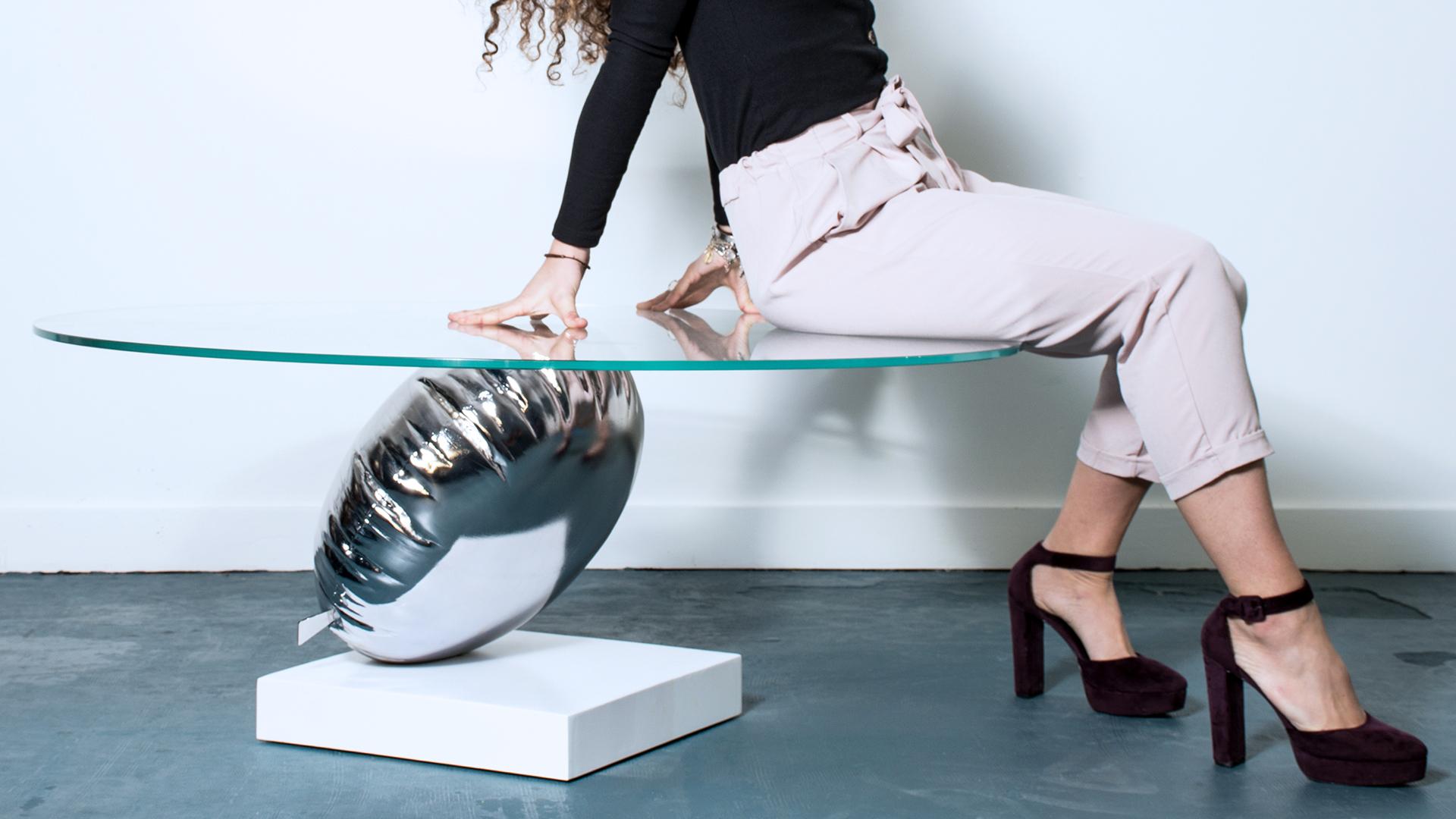 A modern furniture statement piece, the Balance coffee table by Duffy London.

A single silver Helium balloon standing on a thin white disc gives a playful trompe l’oeil, holding a large piece of glass at a perfectly level and balanced state, that