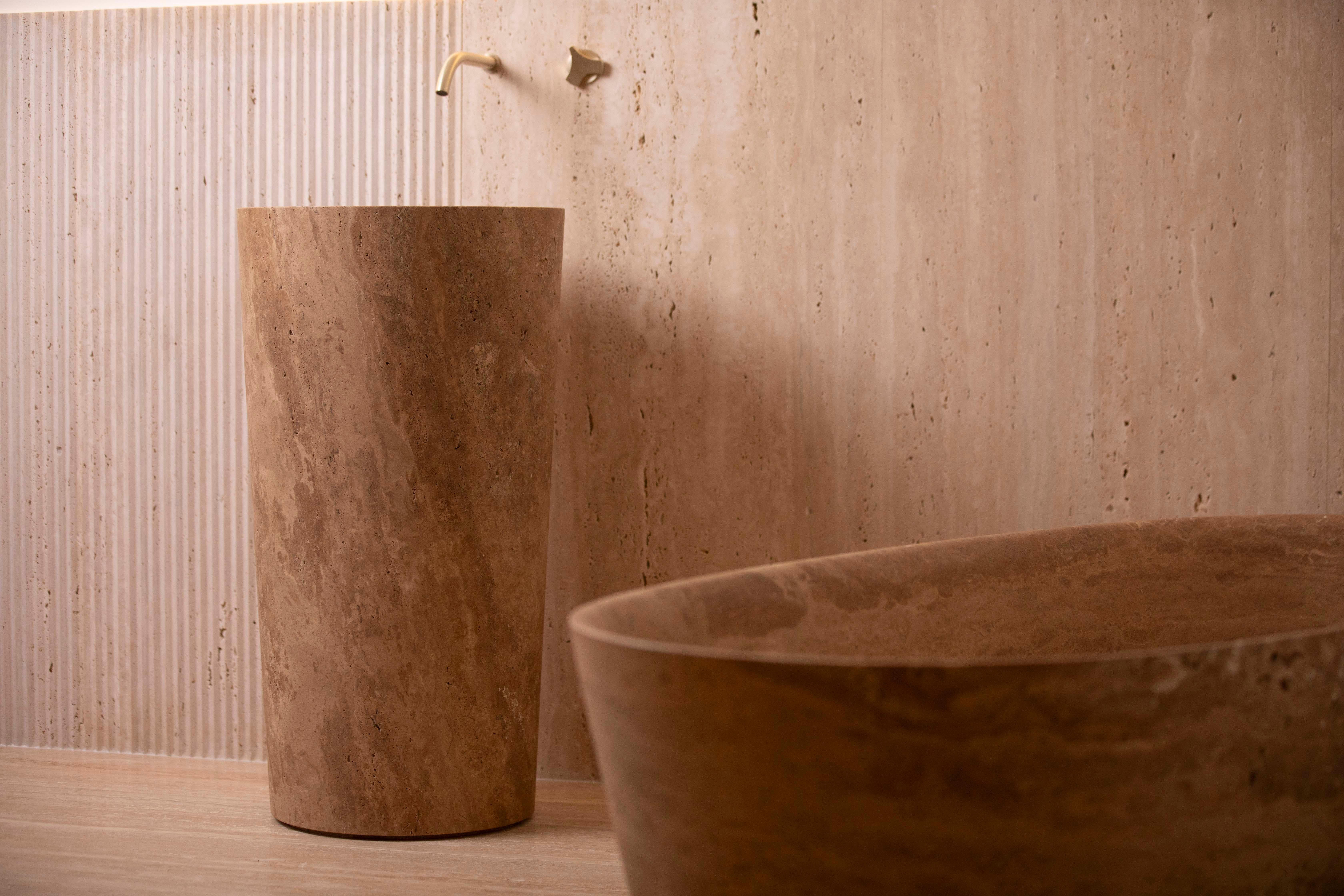 Der Waschtisch Balde Colonna ist eine atemberaubende Verkörperung modernen Designs, bei dem elegante geometrische Linien mit der zeitlosen Schönheit von Naturstein verschmelzen. Dieses skulpturale Stück wird aus exquisitem Mandel-Travertin gefertigt