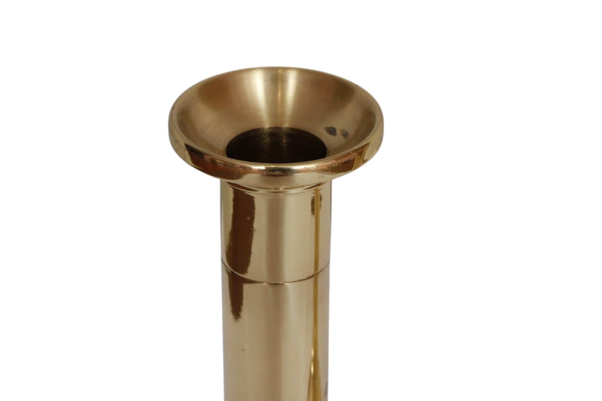 A pair of contemporary brass candlestick holders made in the United States by Baldwin. Sleek columns with sleek wax pans have capitals defined with a single beveled line. Round bases are lightly rippled.

Baldwin entered the home decor business in