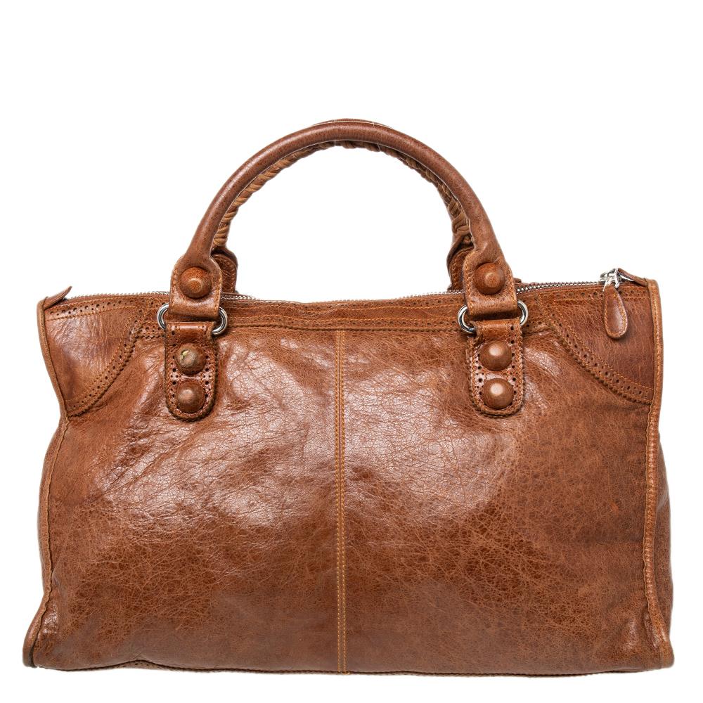 This Balenciaga Work tote is perfect for everyday use. Crafted from brogue leather in a gorgeous hue, the bag has a feminine silhouette with two top handles and a front zip pocket. The zip closure opens to a fabric-lined interior that will hold all