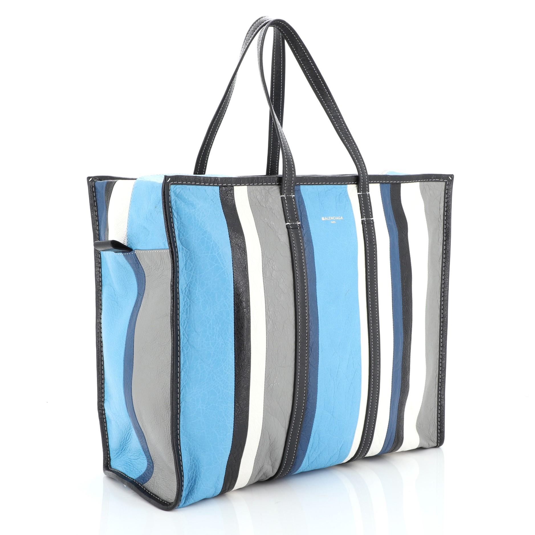 This Balenciaga Bazar Tote Striped Leather Large, crafted in blue and multicolor striped leather, features dual flat leather handles and silver-tone hardware. Its zip closure opens to a black fabric interior with zip and slip pockets. 

Estimated