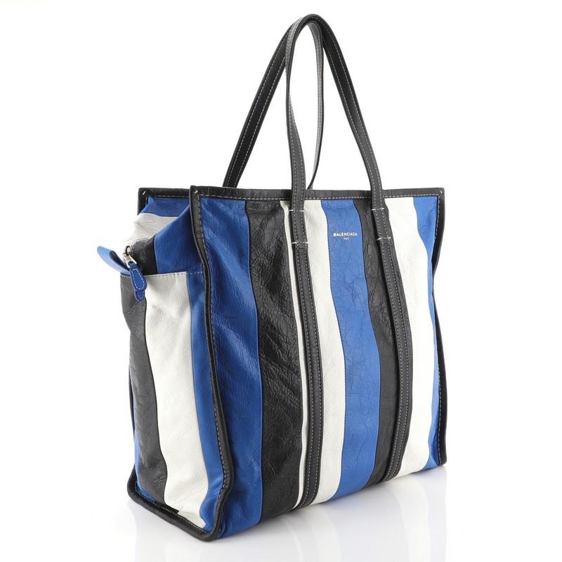 This Balenciaga Bazar Tote Striped Leather Medium, crafted in blue multicolor striped leather, features dual flat leather handles, contrast stitching, and silver-tone hardware. Its zip closure opens to a black fabric interior with zip and slip