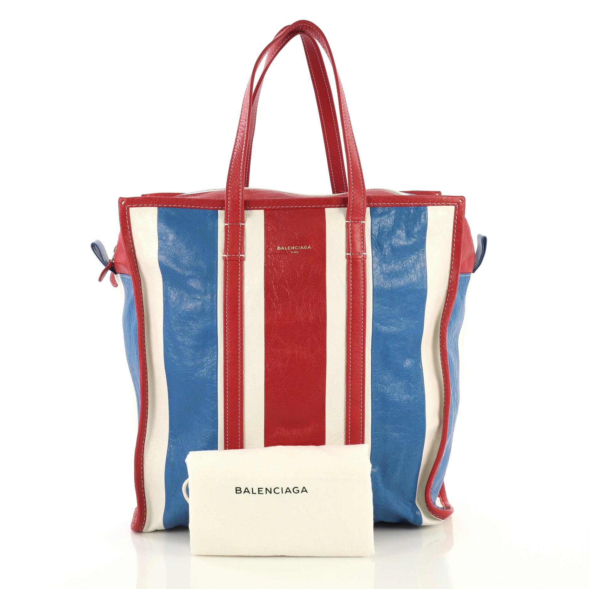 This Balenciaga Bazar Tote Striped Leather Medium, crafted in white, red and blue striped leather, features dual flat leather handles, contrast stitching, and silver-tone hardware. Its zip closure opens to a black fabric interior with zip and slip
