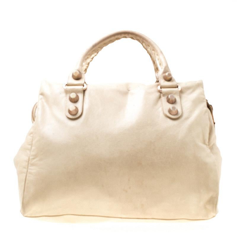 A popular bag among celebrities, this Giant 21 Midday bag by Balenciaga will never leave you unnoticed! It is crafted from muted beige leather and is accented with oversized signature metal buckle and stud details at the front. It comes with a