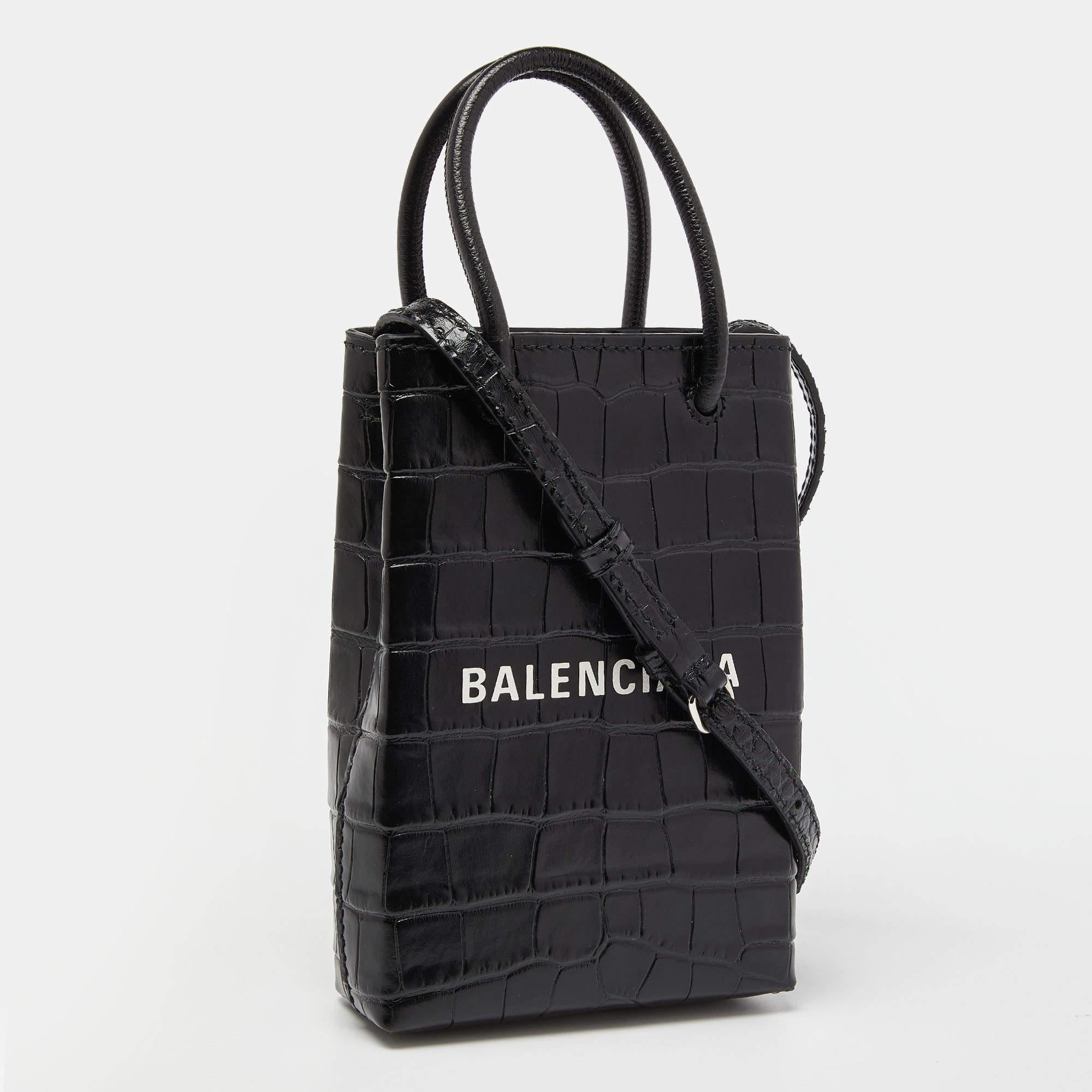 The Balenciaga crossbody bag is a luxurious accessory. Crafted from high-quality black crocodile-embossed leather, it features a sleek, compact design with a phone pocket, card slots, and a detachable crossbody strap for hands-free convenience. It