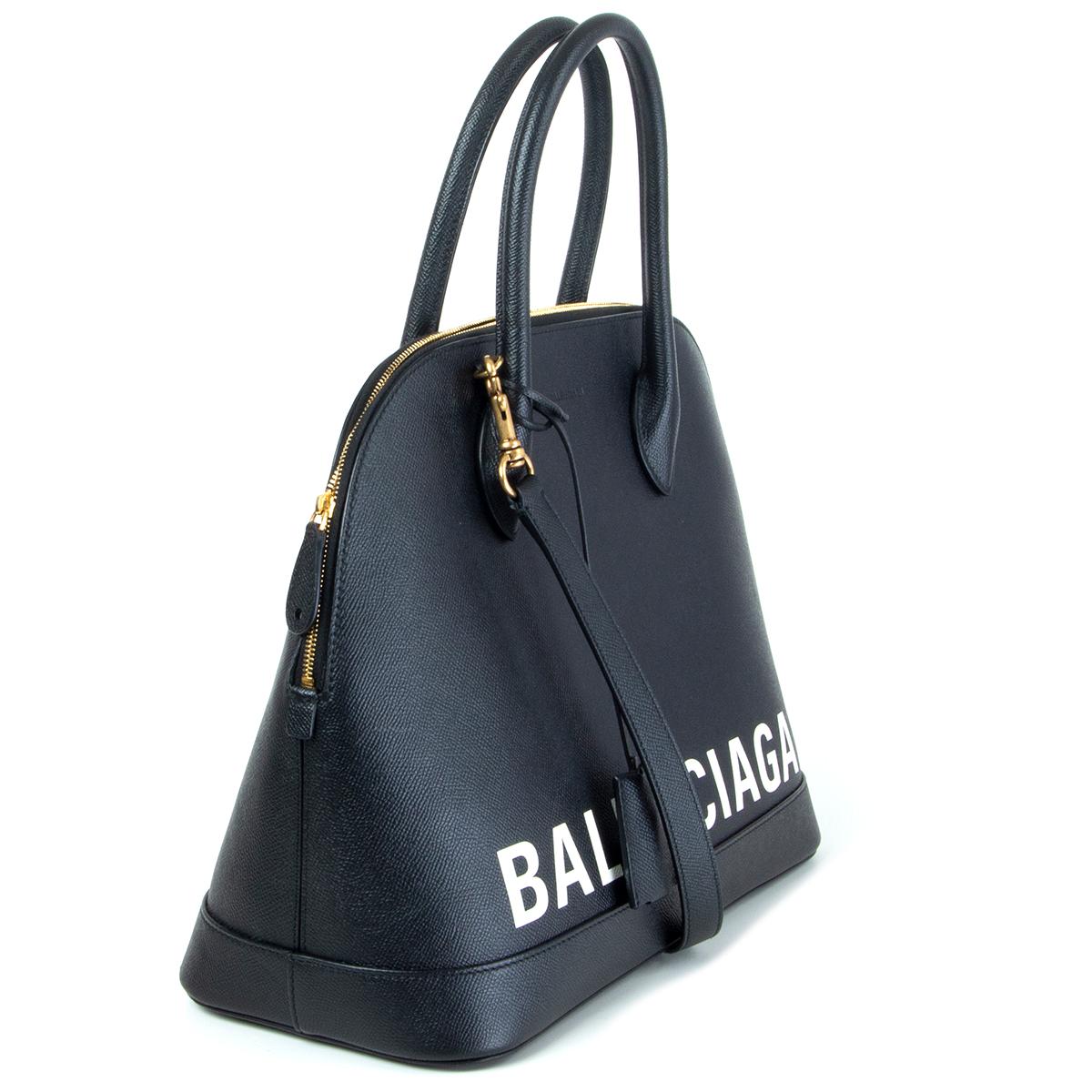 authentic Balenciaga Ville Medium graffiti logo bag in black grained calfskin with large white graffiti inspired Balenciaga front logo. Opens with a top zip fastening with padlock and key. Has a back patch pocket and a removable and adjustable
