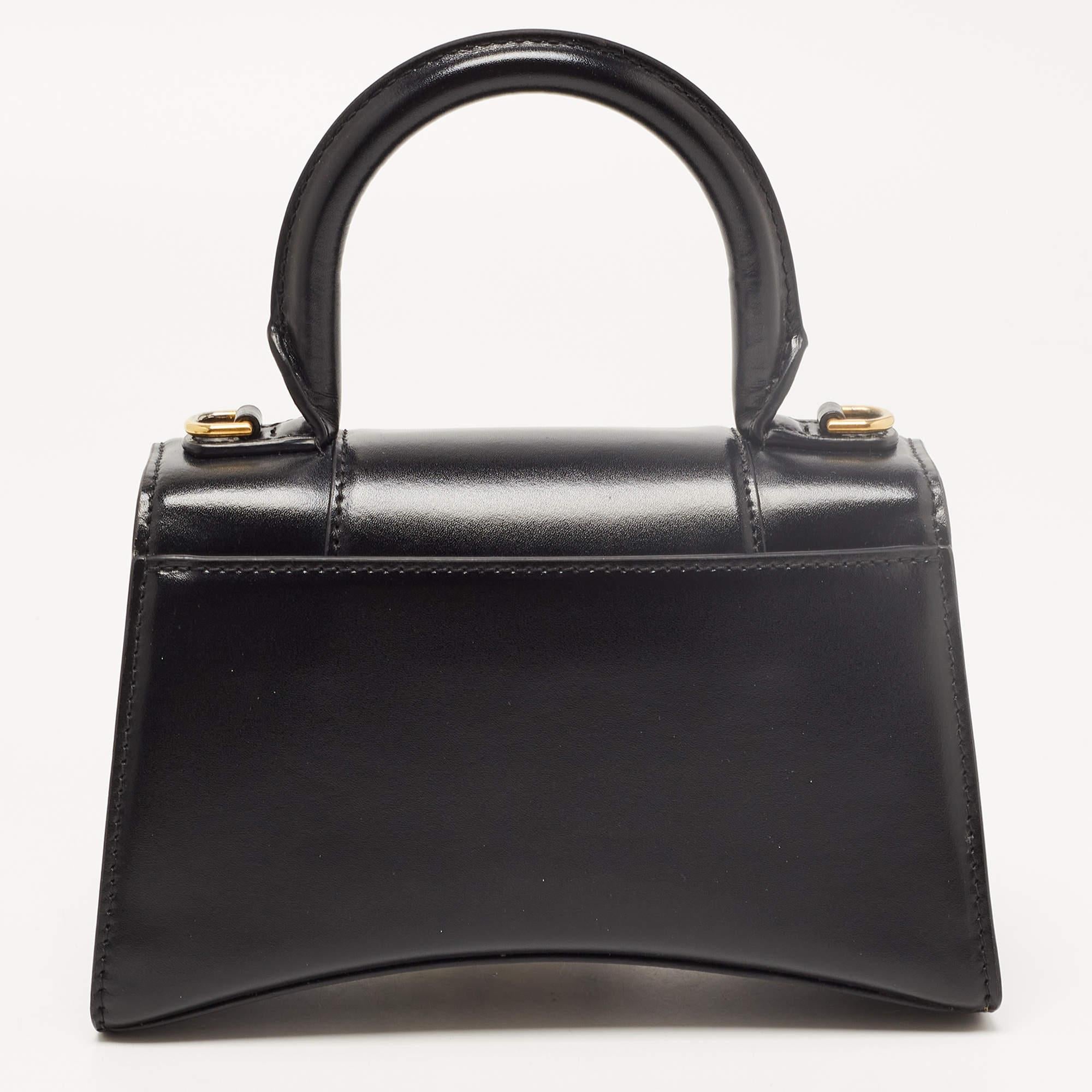 Balenciaga's Hourglass bag is a must-have bag. Crafted using black leather, the Hourglass top handle bag is styled with a flap that has the iconic B logo. The bag has a lined interior, a shapely top handle, and a shoulder strap.

Includes: Original