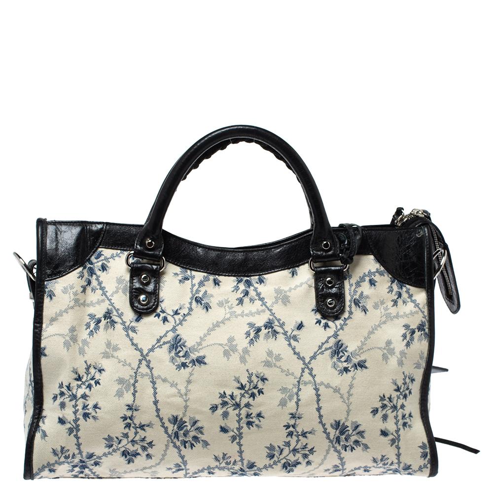 Make an impressive style statement by carrying this classy bag from the house of Balenciaga. Made with fabric & leather, it looks stylish when teamed with the right outfits. Its zipper closure on the top and buckle detail, and floral motifs are the