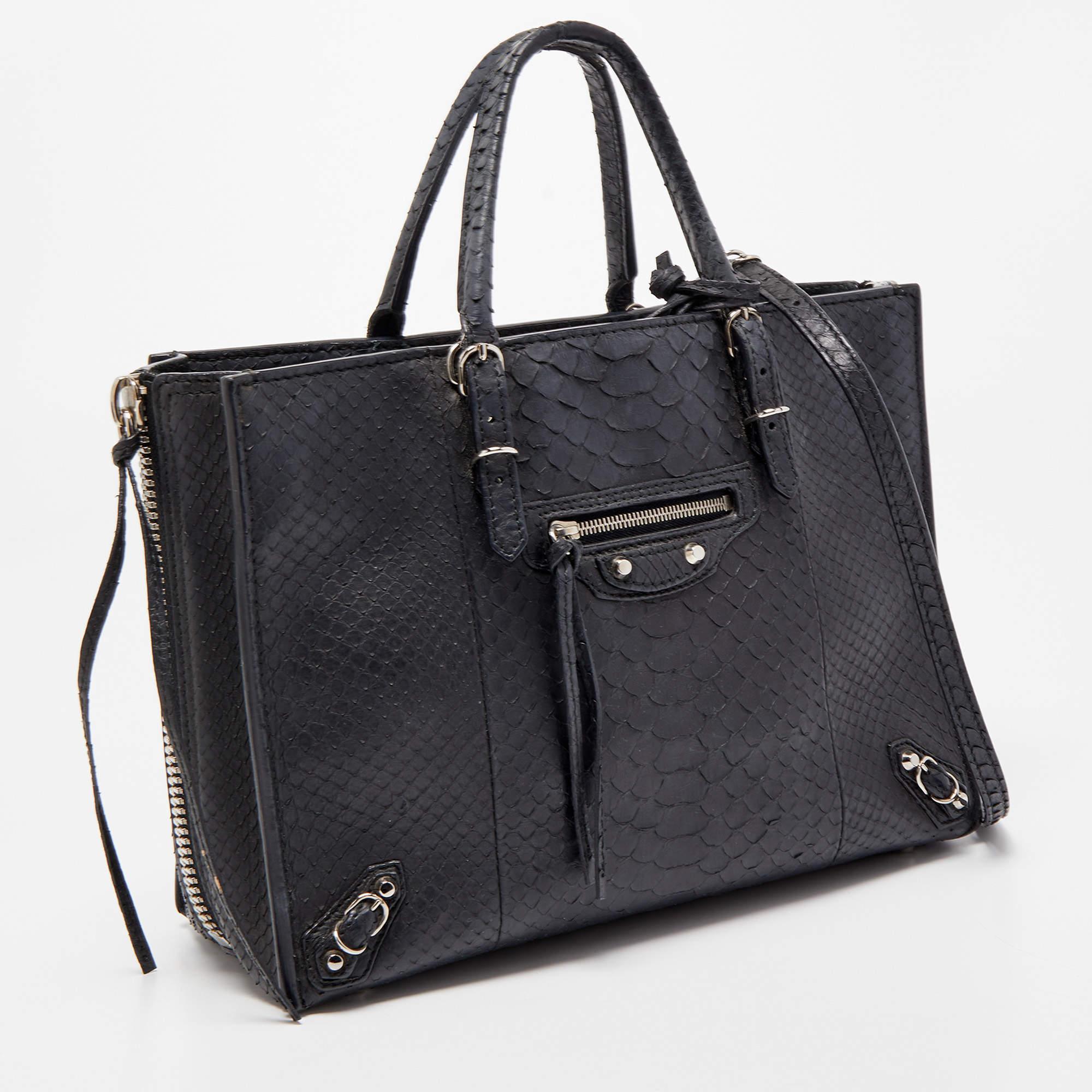 Die Tasche Papier A6 von Balenciaga verbindet Luxus mit praktischer Mode. Sie ist aus Pythonleder gefertigt und verfügt über zwei obere Griffe, eine Innenausstattung aus Leder und einen Taschenspiegel. Die Reißverschlüsse und Schnallendetails machen