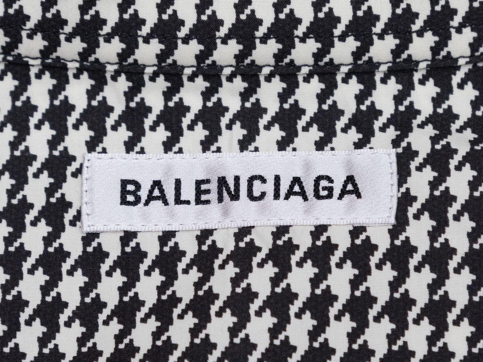 Product Details: Black and white houndstooth print long sleeve button-up top by Balenciaga. Pointed collar. Button closures at center front. Designer size 34. 50