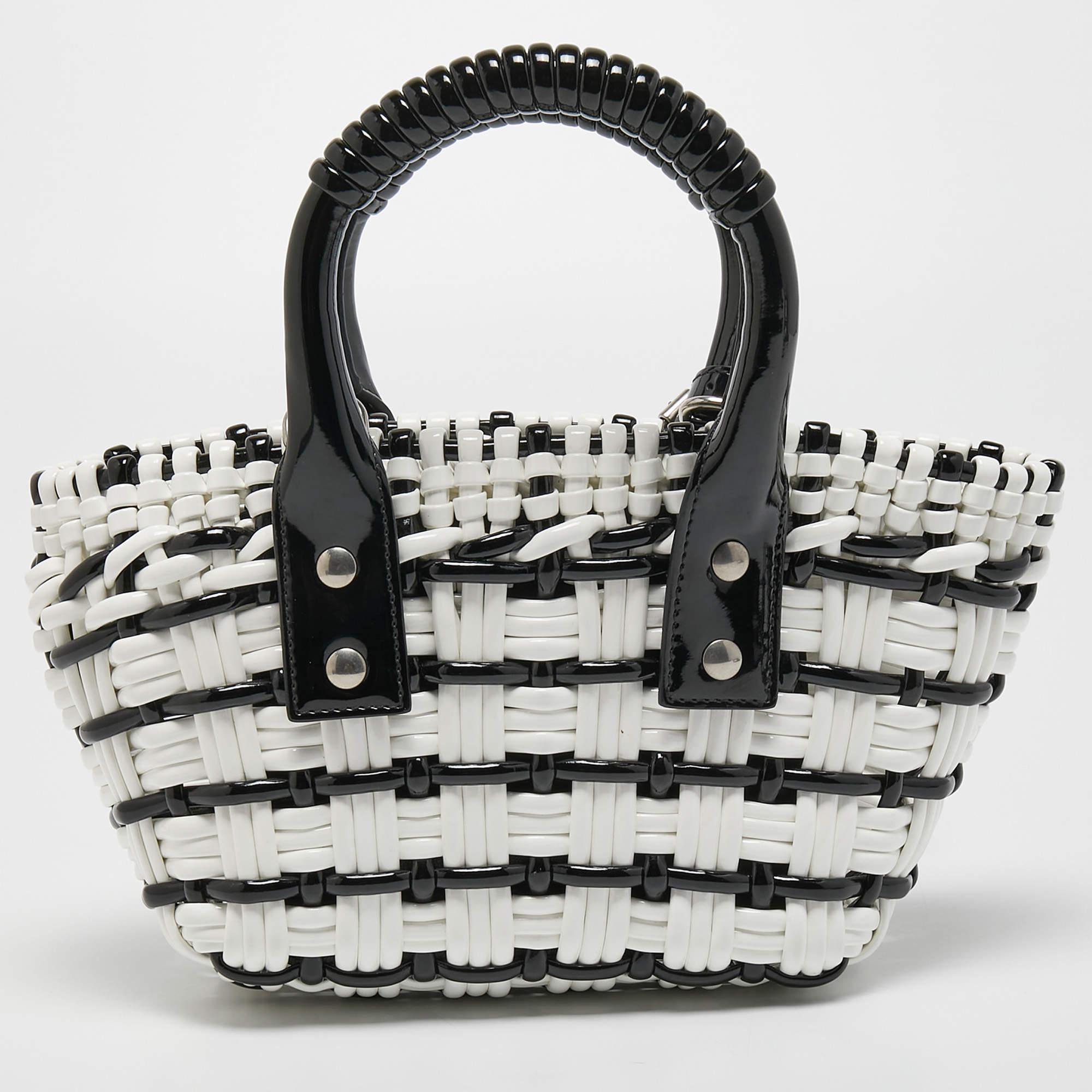The Balenciaga Bistro tote is a stylish and sophisticated handbag. Made from high-quality patent leather, it features a unique woven design in black and white. The tote has a spacious interior with a zippered pocket and a magnetic closure to keep