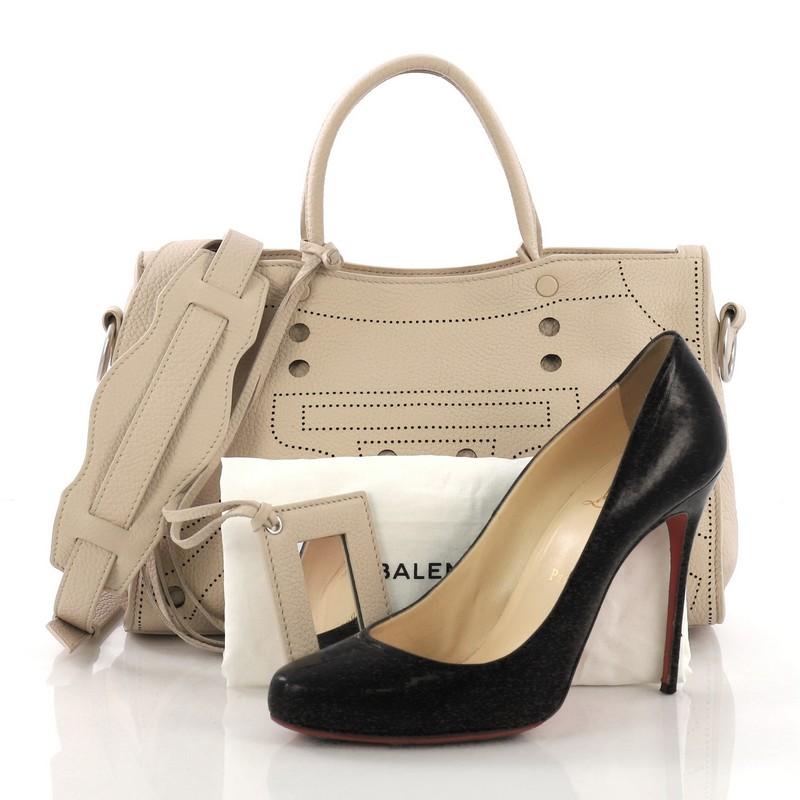 This Balenciaga Blackout City AJ Handbag Leather Small, crafted in beige leather, features dual-rolled leather handles with magnetic base, detachable strap, perforated trims, and silver-tone hardware. Its zip closure opens to a beige leather