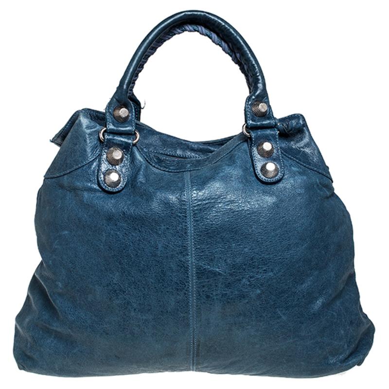 A popular bag among celebrities, this Midday bag by Balenciaga will never leave you unnoticed! It is crafted from blue leather and is accented with oversized signature metal buckles and stud details on the front. It comes with a matching leather