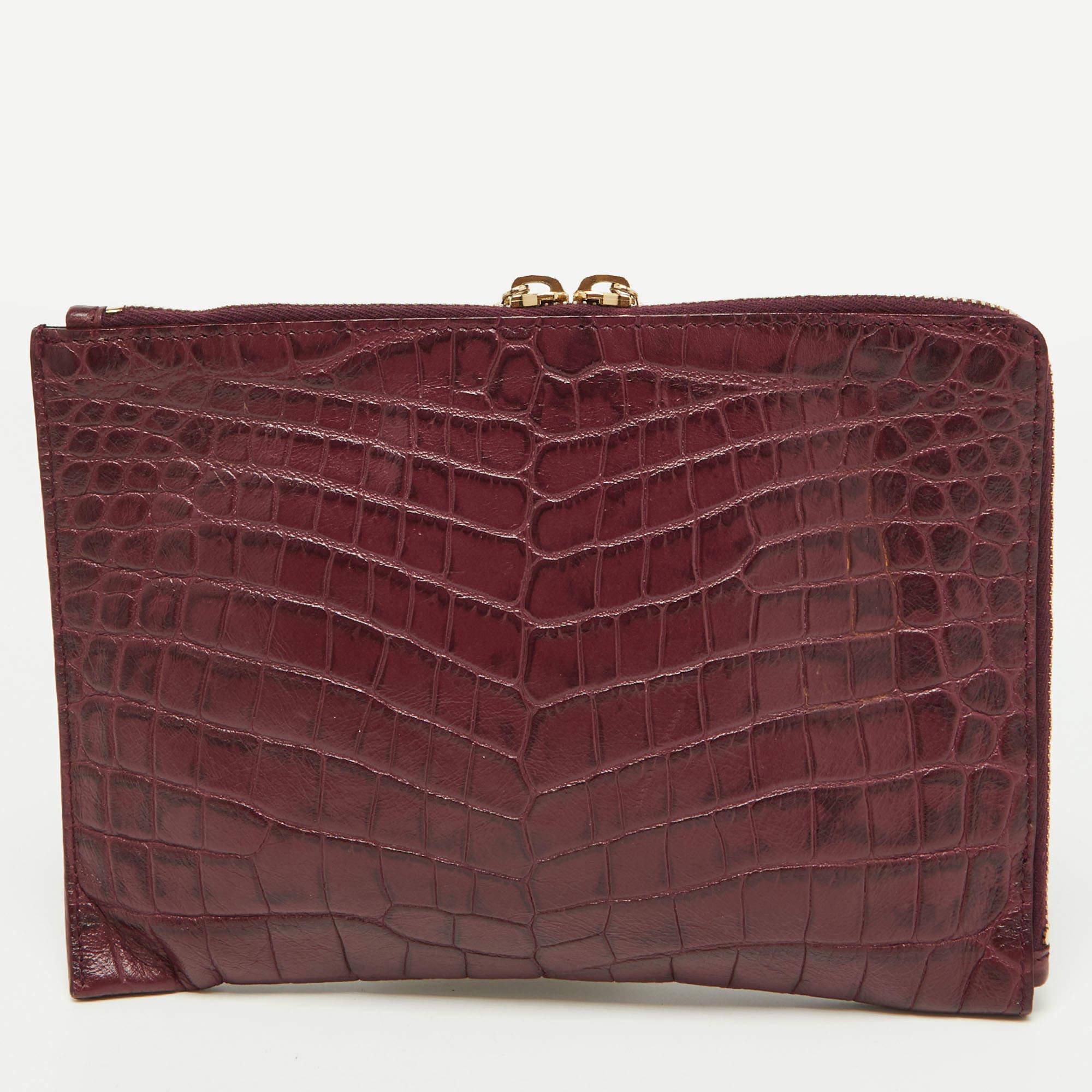 This pretty Balenciaga clutch is a stylish creation that is exceptionally well-made. This clutch is crafted from croc-embossed leather and accented with signature gold-tone studs, corner buckle detailing, and a front zip pocket. The interior is