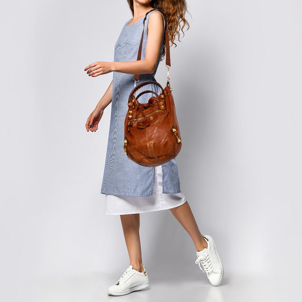 Diese SGH Pompon Hobo von Balenciaga kommt im Eimer-Stil daher. Die wunderschöne Tasche ist aus braunem Leder gefertigt und wird von zwei oberen Griffen und einem abnehmbaren Schulterriemen gehalten. Die Hobo hat goldfarbene Beschlagdetails und