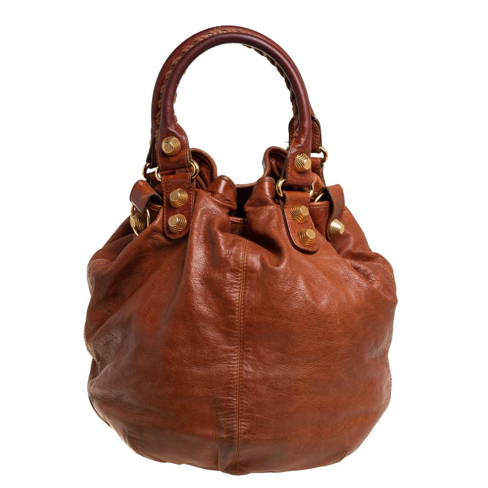 This Balenciaga SGH Pompon hobo arrives in a bucket-style design. The gorgeous bag is made from brown leather and is held by two top handles and a detachable shoulder strap. The hobo has gold-tone hardware details and a spacious interior sized to