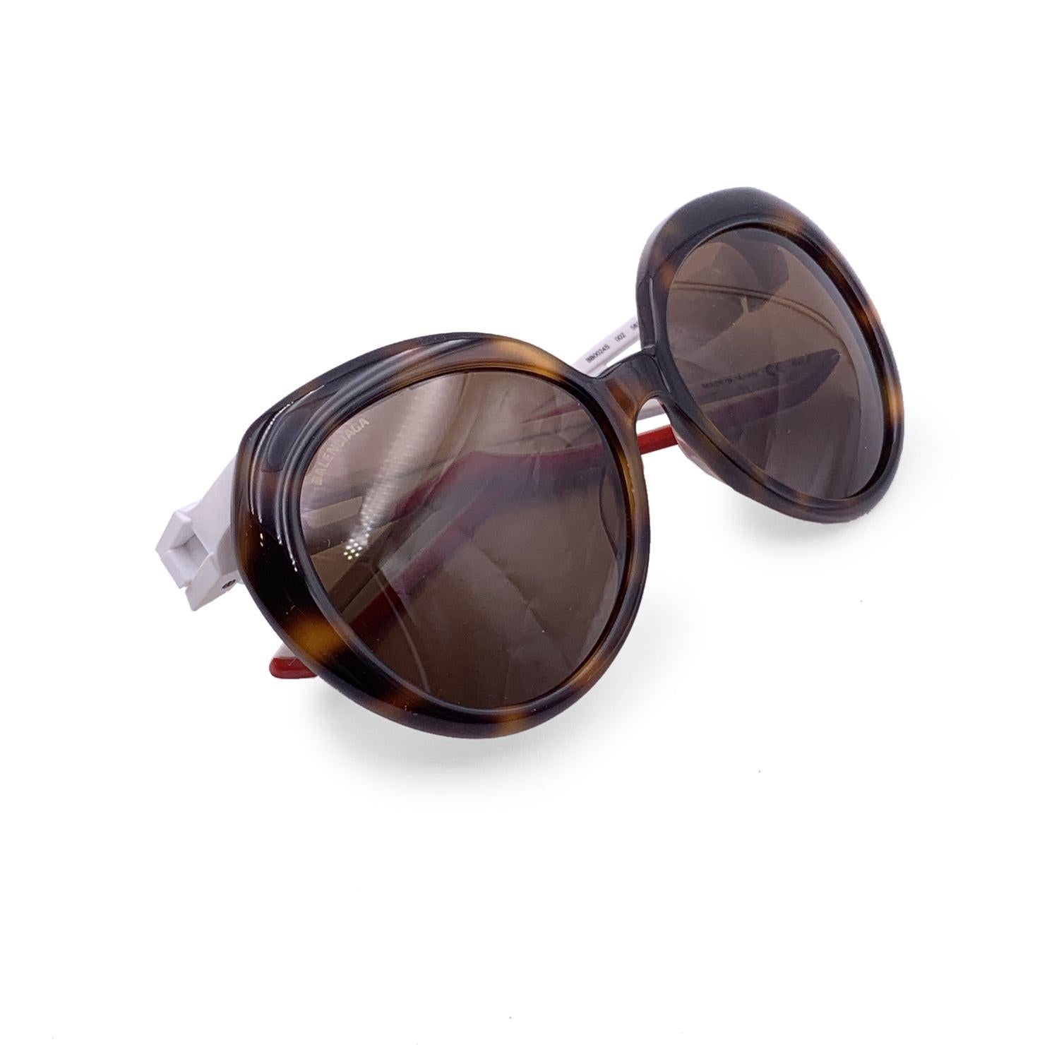 Balenciaga TripleS BB0024S sunglasses in color 002 brown. Oversizedbrown havana oval frame and brown lenses. White and red rubber effect temples with a black logo. Mod & refs: BB0024S - 002 - 58/19 - 135. Made in Italy Details MATERIAL: Plastic