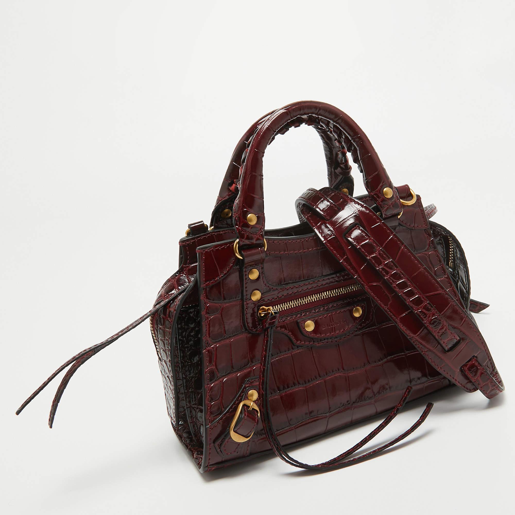 Crafted with finesse, the Balenciaga Neo Classic Bag epitomizes elegance. Luxurious croc-embossed leather in a rich burgundy hue exudes opulence. Its compact silhouette, adorned with studs, makes it a timeless accessory for any discerning fashion