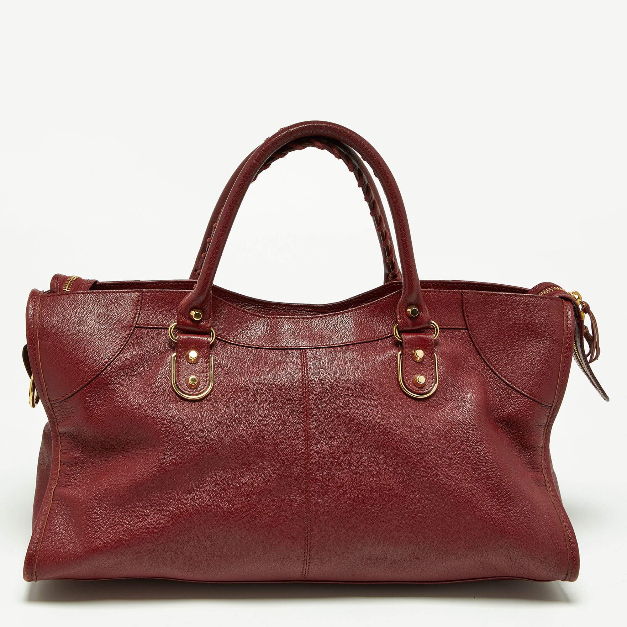 The burgundy exterior of this Balenciaga City bag is made chic and highly fashionable with gold-tone accents. Crafted from leather, it is equipped with a front zipper pocket and can be carried with dual handles or a shoulder strap. The fabric