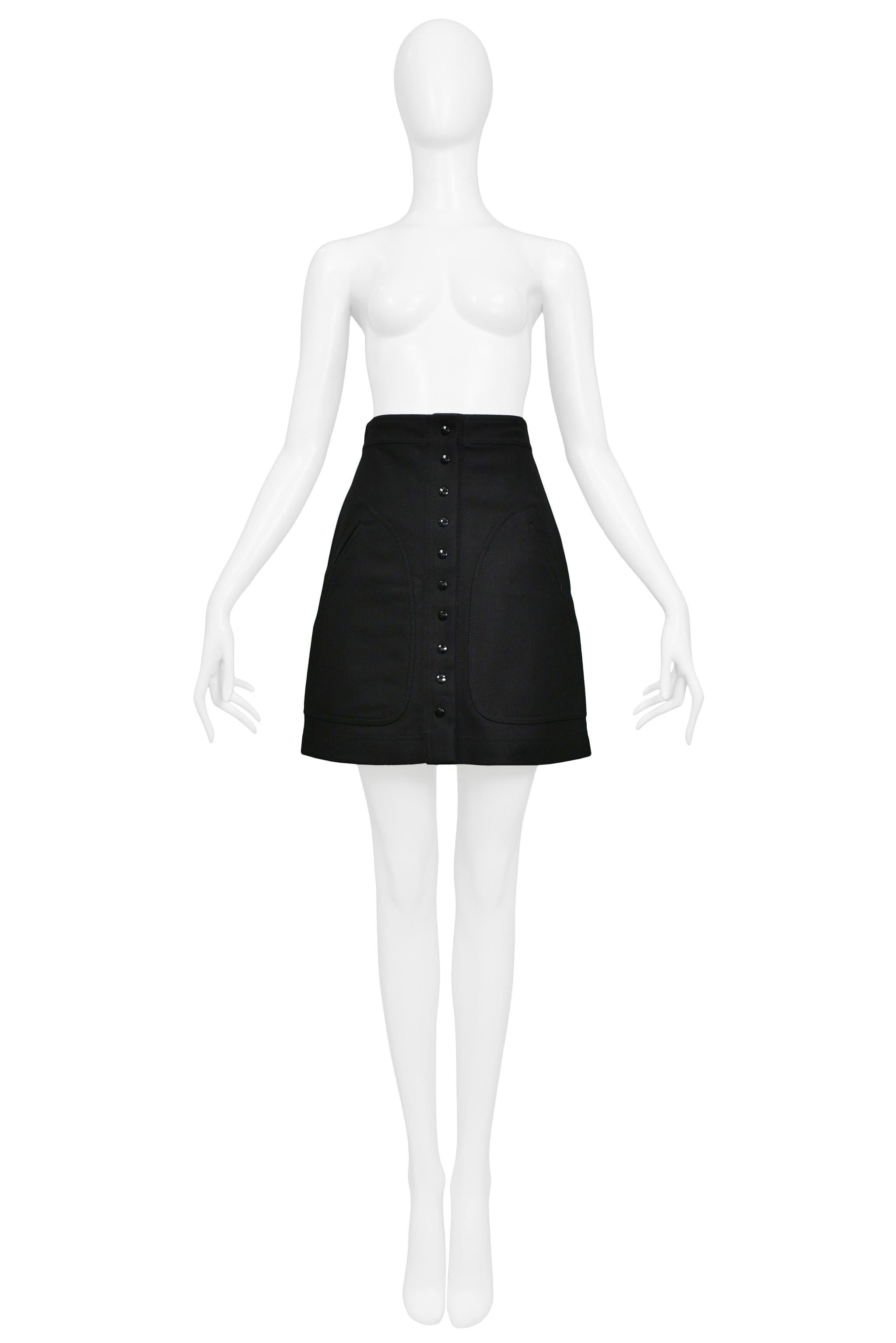 Resurrection Vintage a le plaisir de vous proposer une jupe a-line noire vintage Nicolas Ghesquière avec une taille haute structurée, des boutons-pression noirs au centre du devant de la jupe, et de grandes poches latérales avec des surpiqûres
