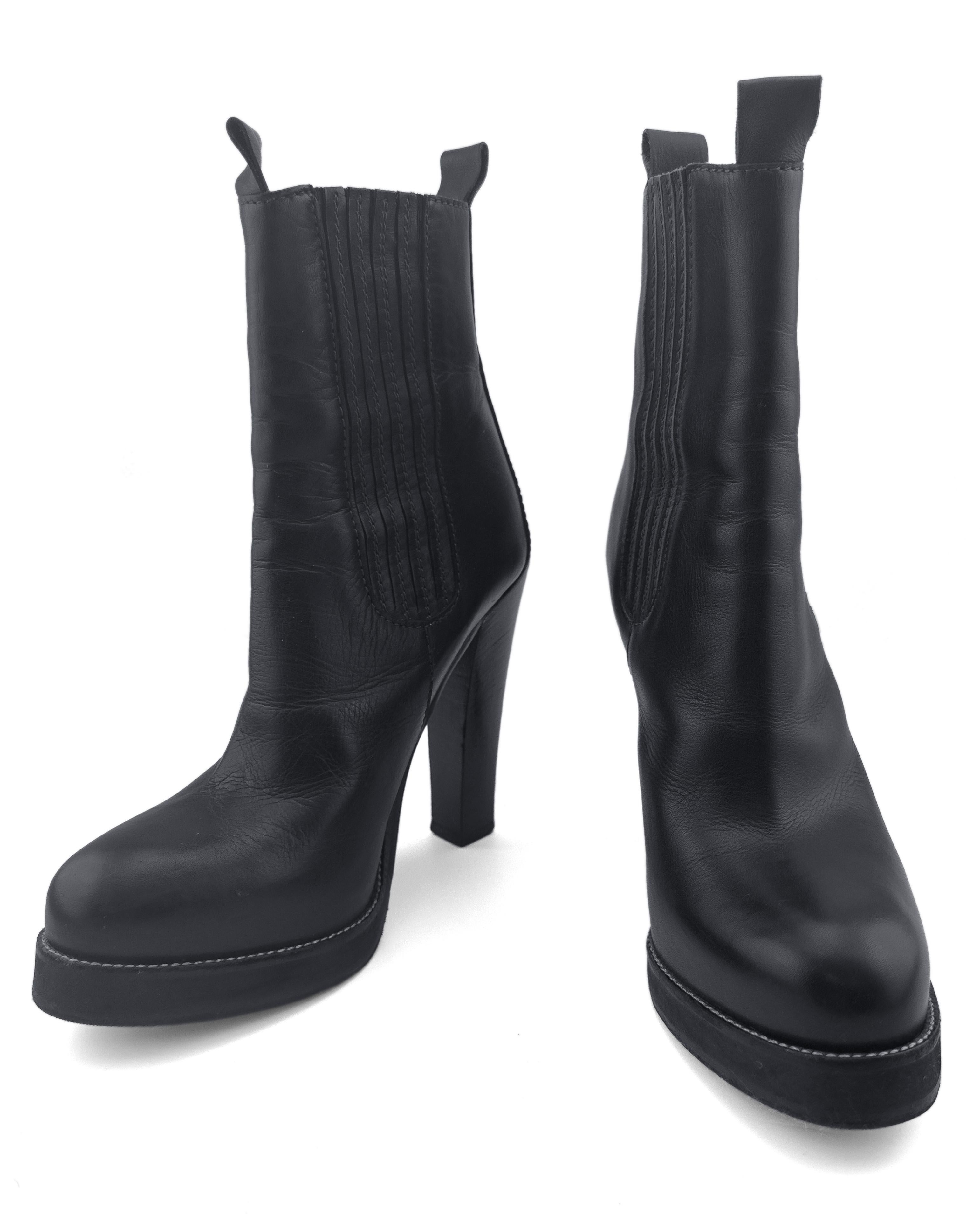 These black leather Chelsea boots from the Fall 2003 runway collection are an ultra-chic fusion of modern minimalism and sculptural power dressing. Crafted in buttery smooth black leather, the design features a sleek high-heeled silhouette with a