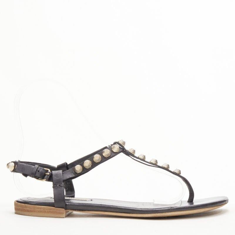 BALENCIAGA Cagole black leather gold textured  stud T-strap flat sandals EU38
Reference: KEDG/A00207
Brand: Balenciaga
Designer: Demna
Material: Calfskin Leather, Metal
Color: Black, Gold
Pattern: Solid
Closure: Ankle Strap
Lining:  Leather
Extra