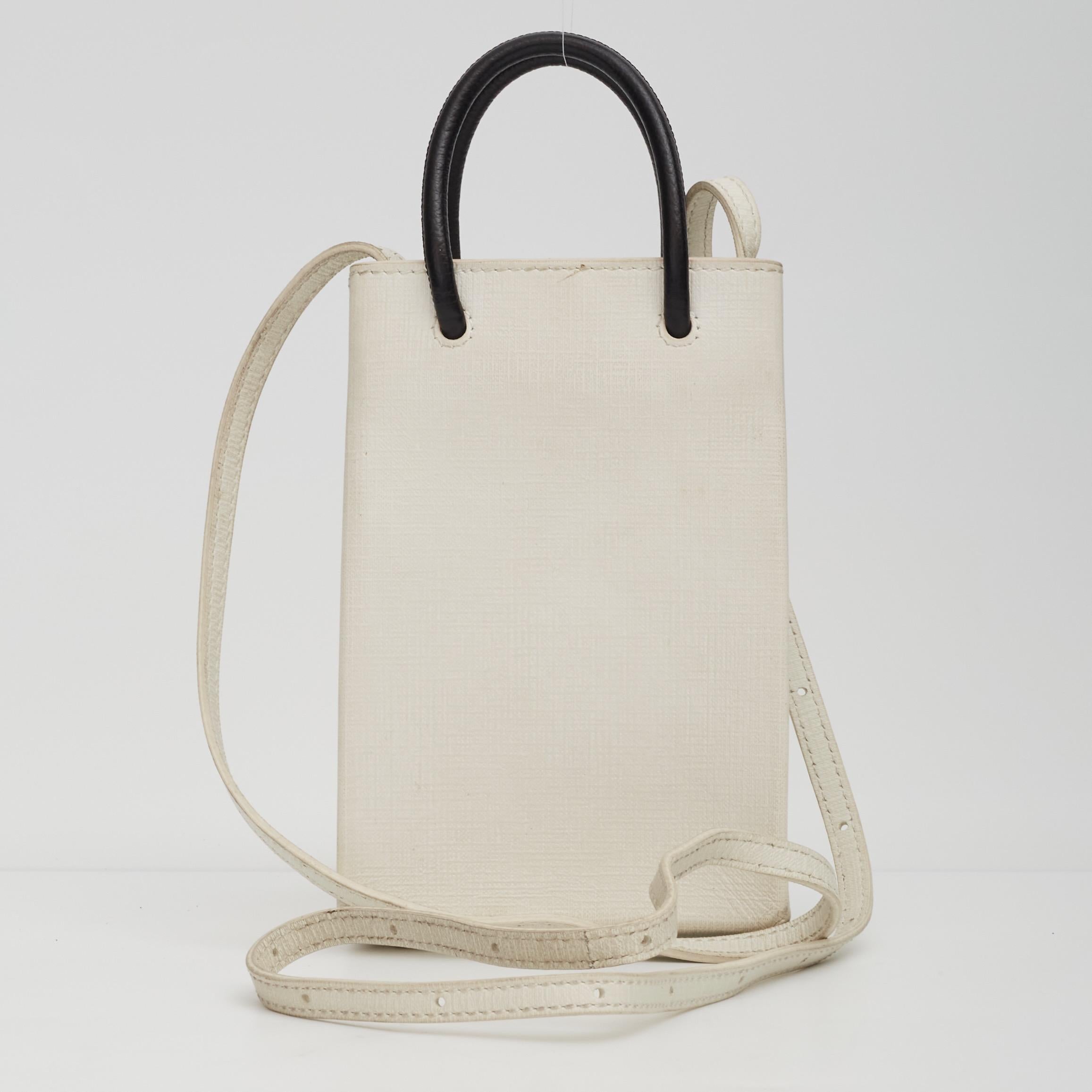 This bag is constructed of white calfskin leather. The bag features dual thin black rolled leather top handles, an adjustable leather crossbody strap, an open top with snap closure and a black fabric interior with a patch pocket.

Color: