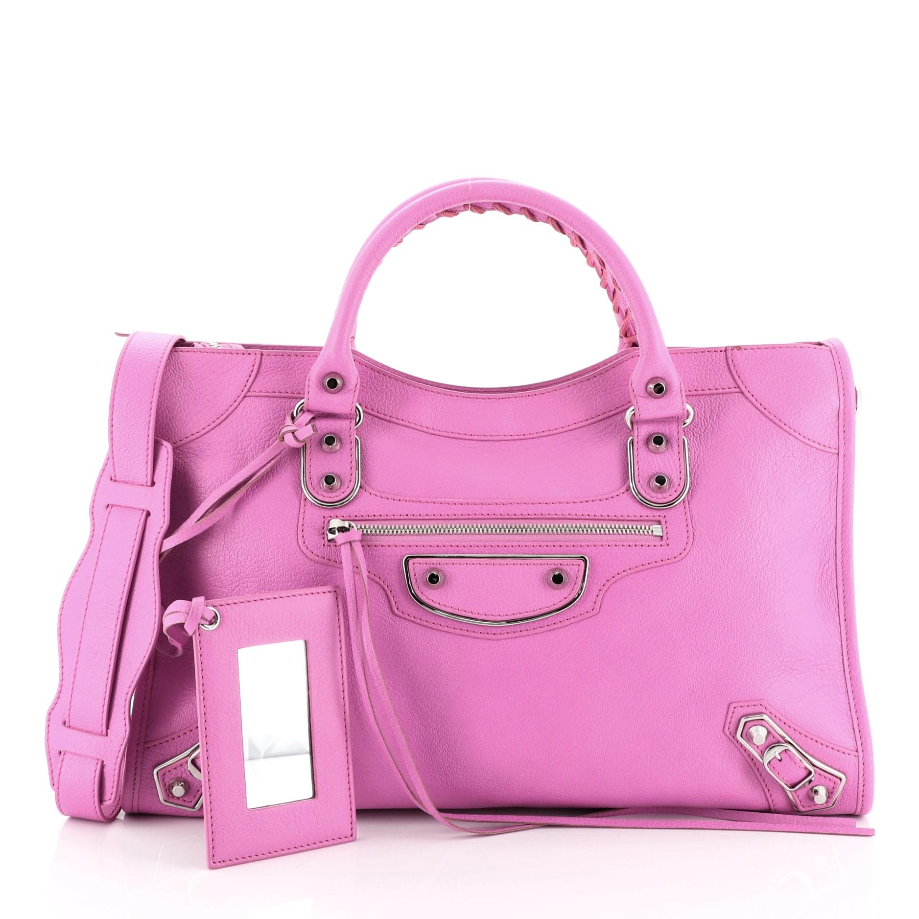 This Balenciaga City Classic Metallic Edge Bag Leather Medium, crafted from pink leather, features dual braided woven handles, studs and buckle details, front zip pocket, and silver-tone hardware. Its top zip closure opens to a black fabric interior