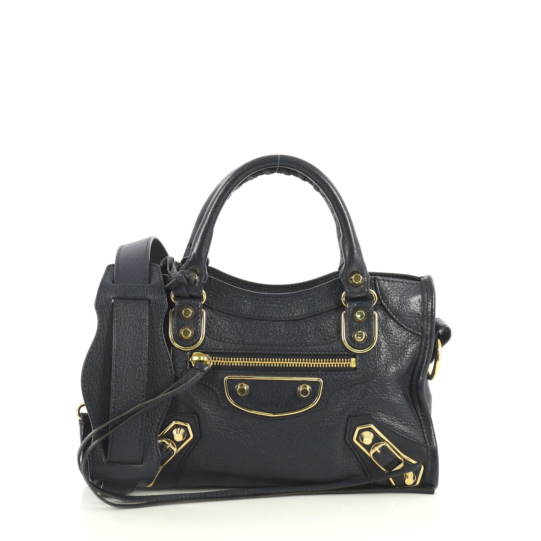 This Balenciaga City Classic Metallic Edge Bag Leather Mini, crafted from blue leather, features dual braided woven handles, studs and buckle details, front zip pocket, and gold-tone hardware. Its top zip closure opens to a black fabric interior