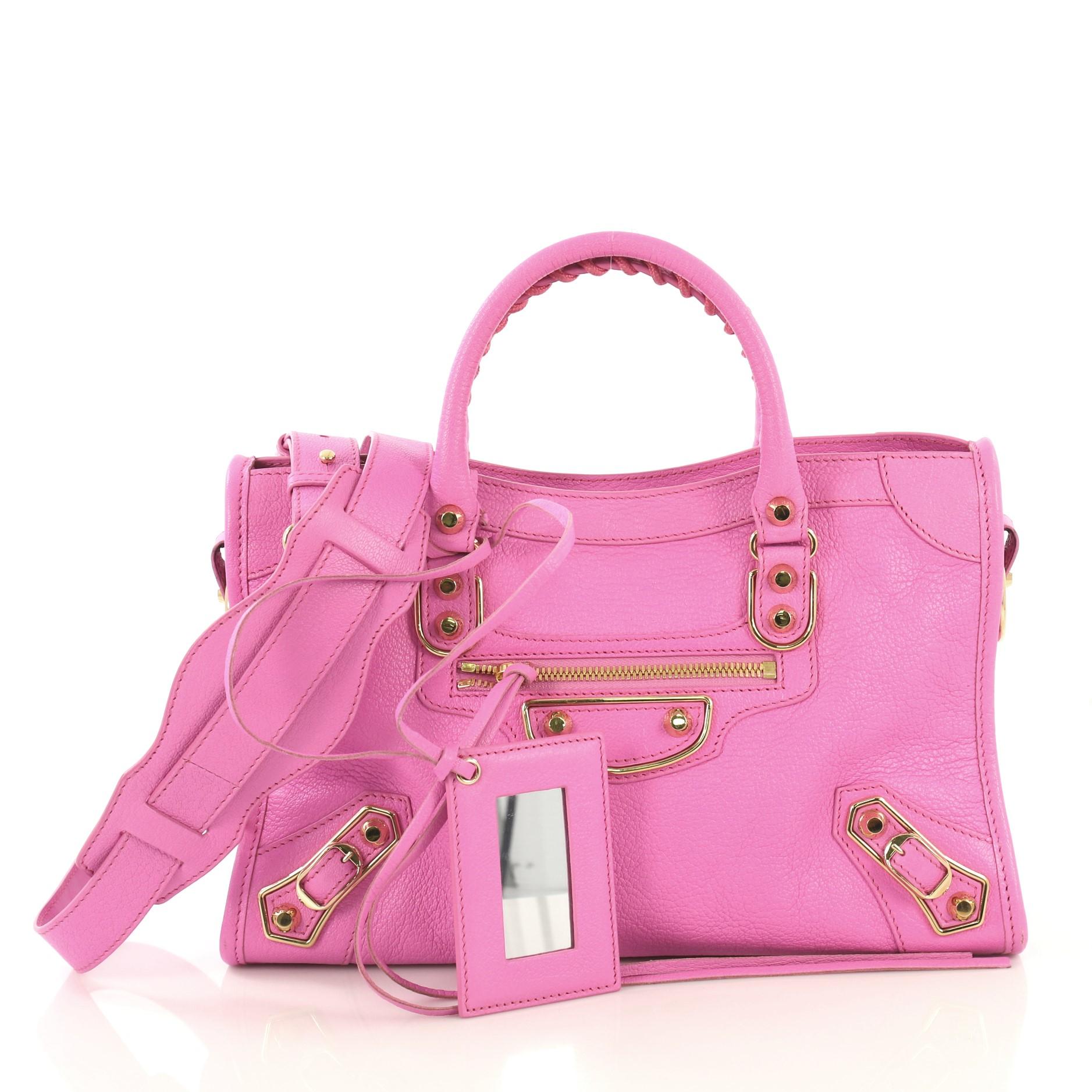 This Balenciaga City Classic Metallic Edge Bag Leather Small, crafted from pink leather, features dual braided woven handles, studs and buckle details, front zip pocket, and gold-tone hardware. Its top zip closure opens to a black fabric interior