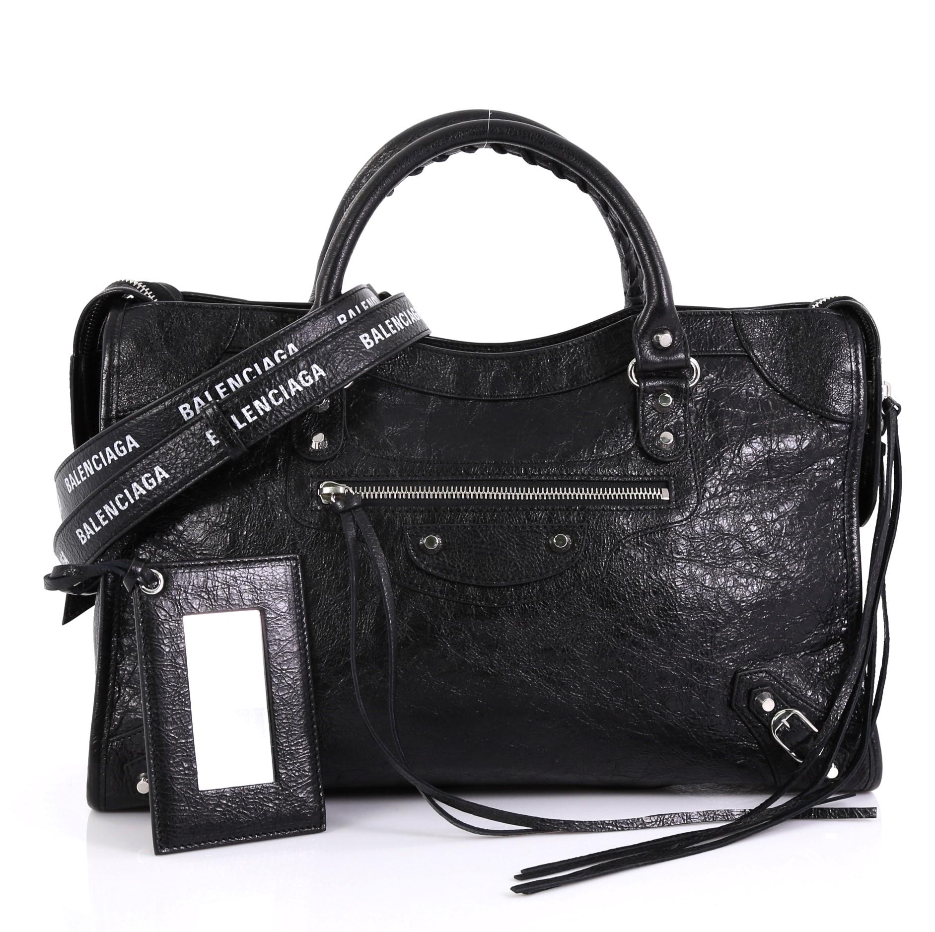 This Balenciaga City Classic Studs Bag Leather Medium, crafted from black leather, features dual braided woven handles, stud and buckle details, exterior front zip pocket, and silver-tone hardware. Its top zip closure opens to a black fabric