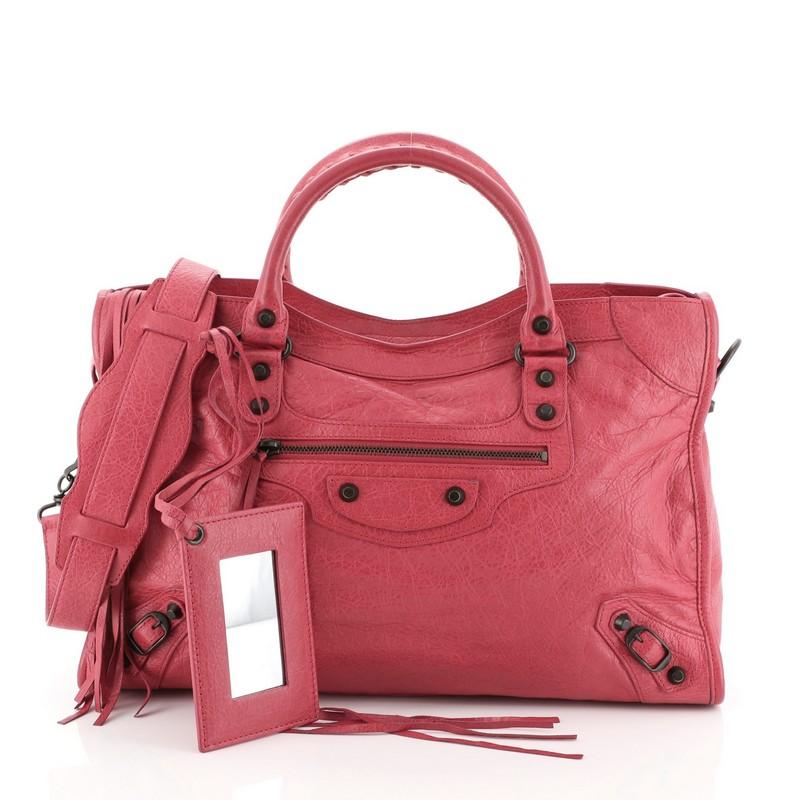 This Balenciaga City Classic Studs Bag Leather Medium, crafted from pink leather, features dual braided woven handles, stud and buckle details, exterior front zip pocket, and brass-tone hardware. Its top zip closure opens to a black fabric interior