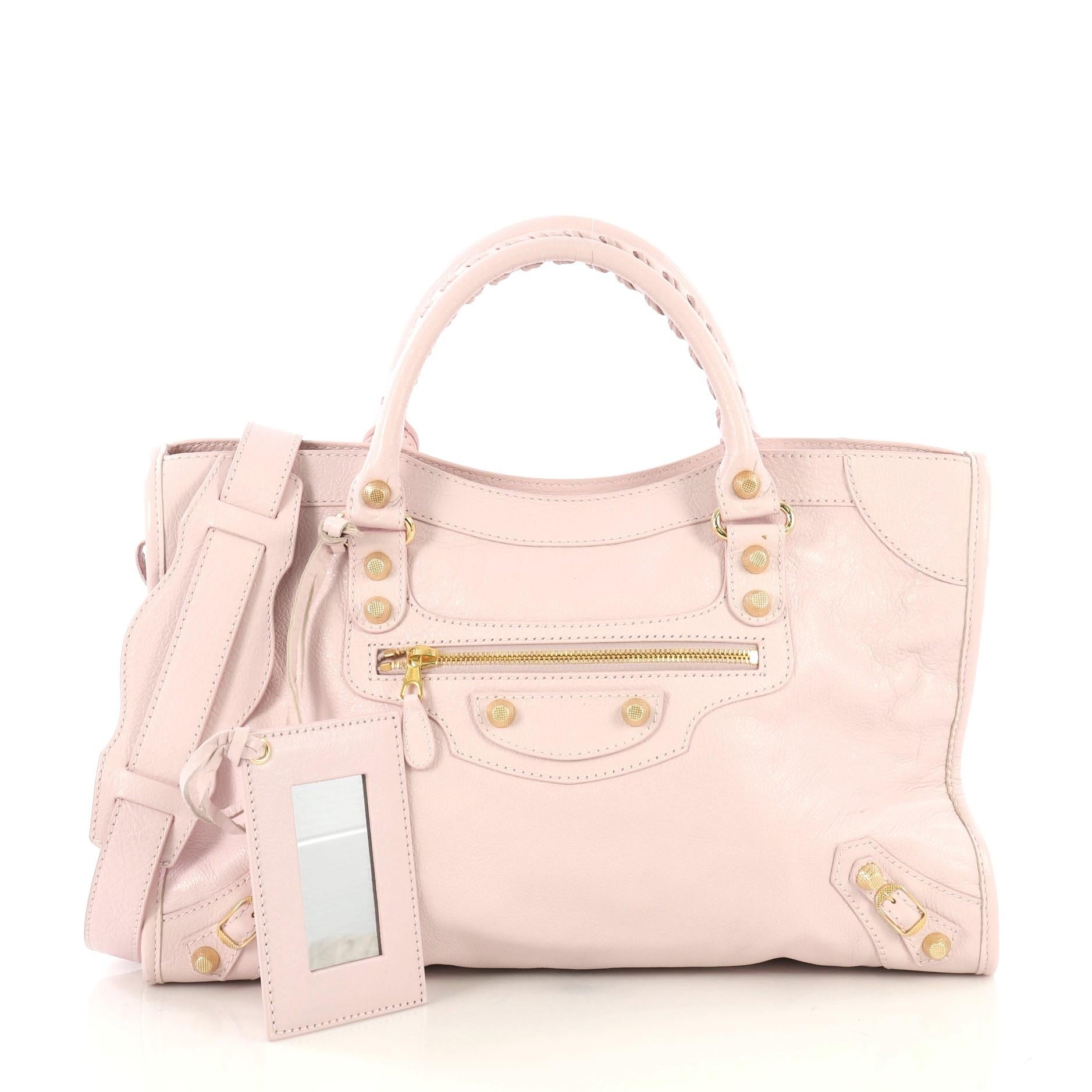 This Balenciaga City Giant Studs Bag Leather Medium, crafted from pink leather, features dual braided woven handles, exterior front zip pocket, stud detailing, and gold-tone hardware. Its top zip closure opens to a black fabric interior with side