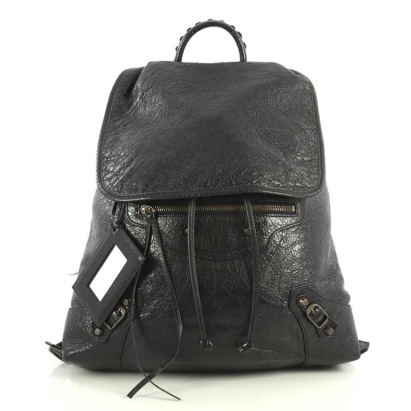 This Balenciaga Classic Traveler Backpack Leather Small, crafted in black leather, features whipstitched top handle, adjustable shoulder/backpack straps, flap over drawstring top with hidden buckle closure, exterior front zip pocket, iconic