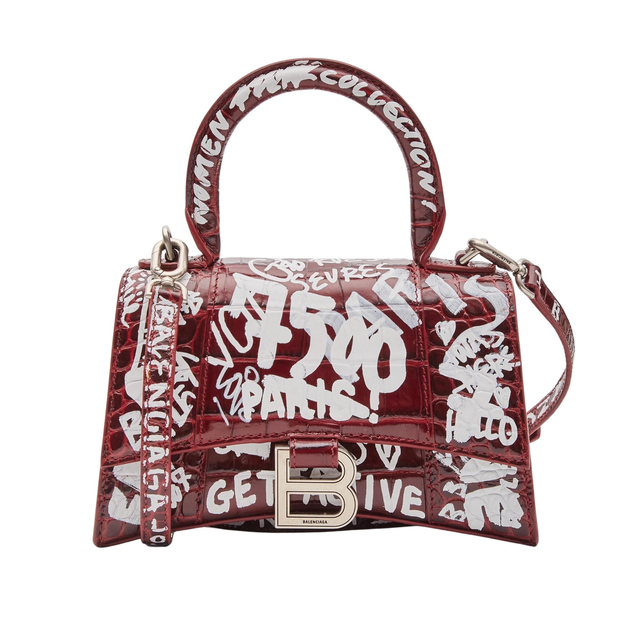 This handbag is made of crocodile embossed burgundy calfskin leather with a white graffiti print overlay. The bag features a sturdy leather top handle with silver links, a prominent b logo on the front flap, and an optional, adjustable shoulder