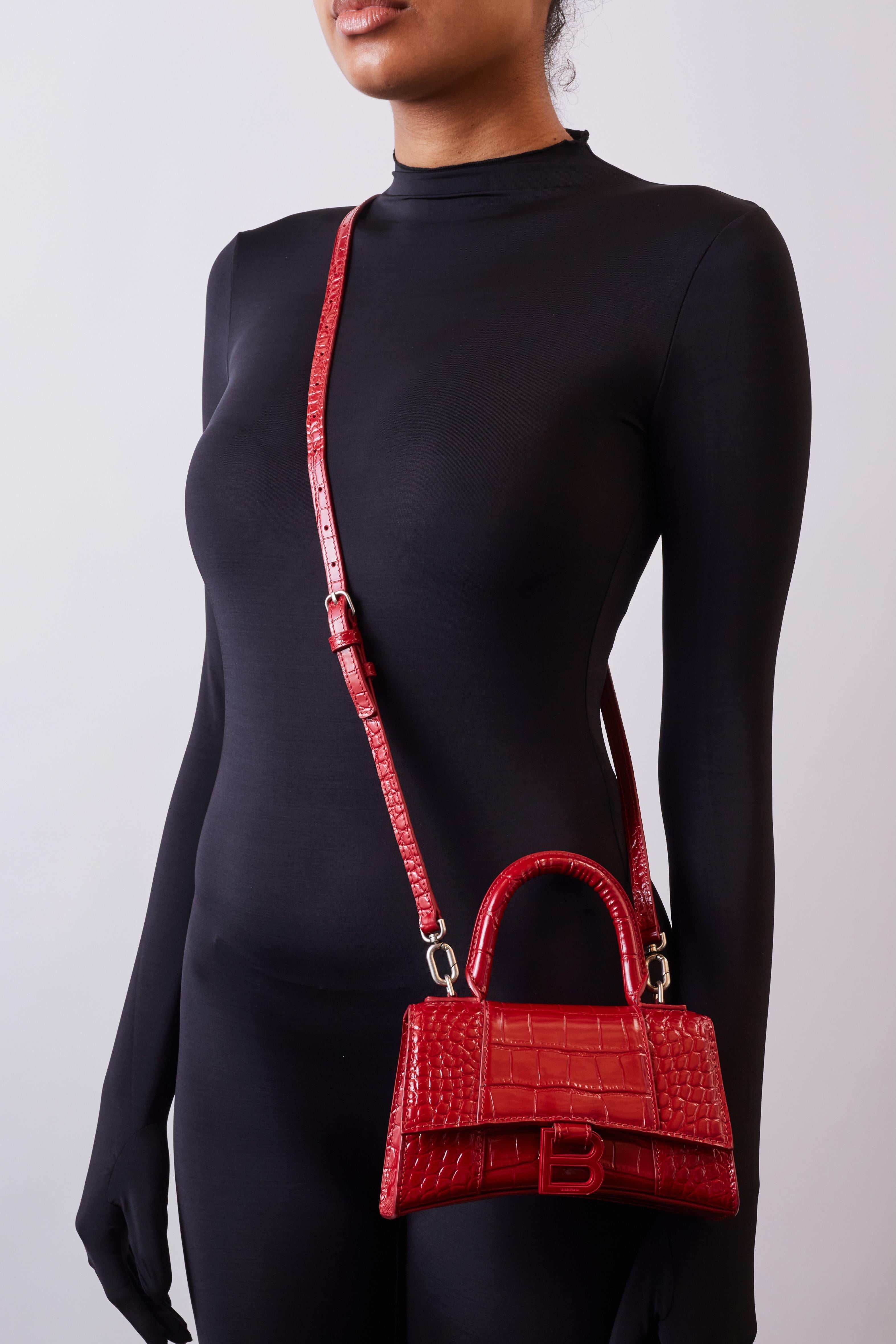This petite handbag is made of crocodile stamped glazed calfskin in bright red. The bag features a top handle and an optional shoulder strap. This bag also features the signature Balenciaga B charm, matte red and silver tone hardware, and slip
