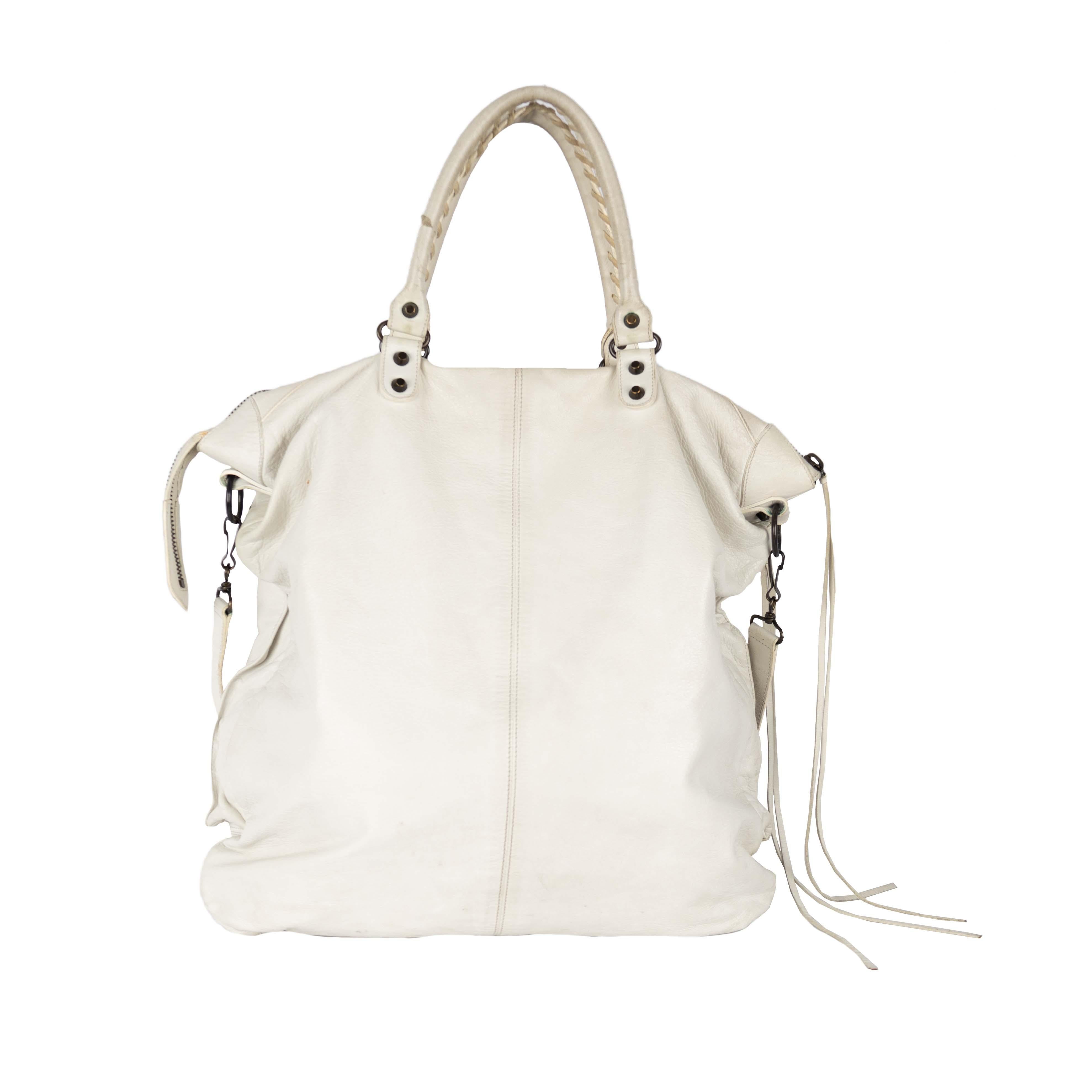 White leather oversized tote bag by Balenciaga with two large front zipped pockets which features long fringes on the zipper. It also includes a mirror. The bag has a long belt for cross body wear and is very spacious, making it perfect as a small