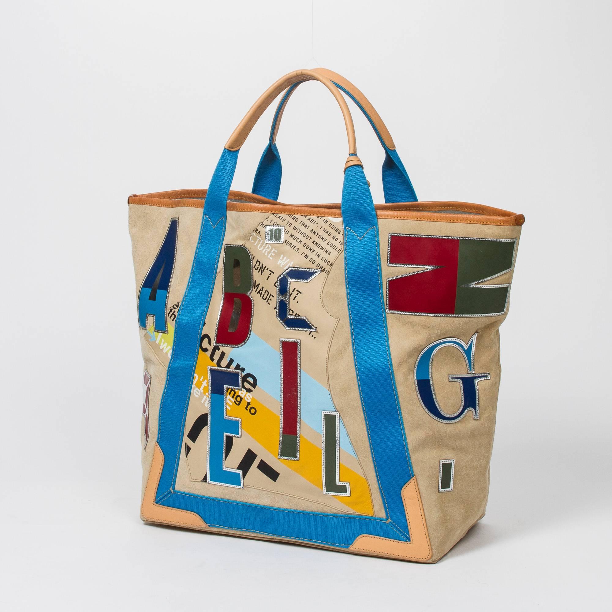 Daim Alphabet Tote in beige suede with beige leather and blue canvas straps, natural hide leather details, silver tone hardware. Metallic silver distressed leather lined interior with one zip pocket. Mirror and dustbag included. Some slight signs of