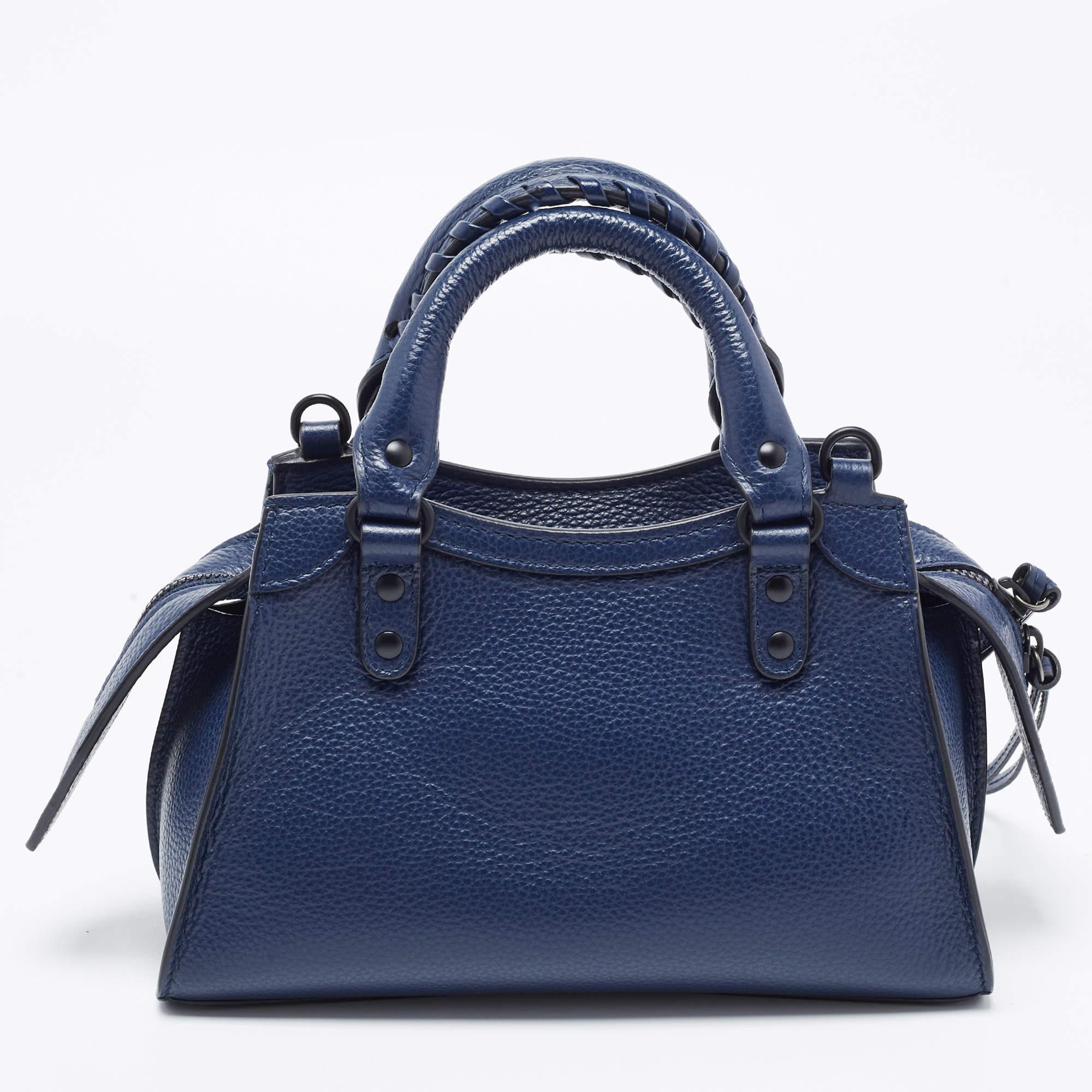 The Balenciaga City tote is a compact yet stylish handbag crafted from premium dark blue leather. It features the iconic Neo Classic design with black-tone hardware, a top zip closure, and a detachable shoulder strap, making it a versatile and