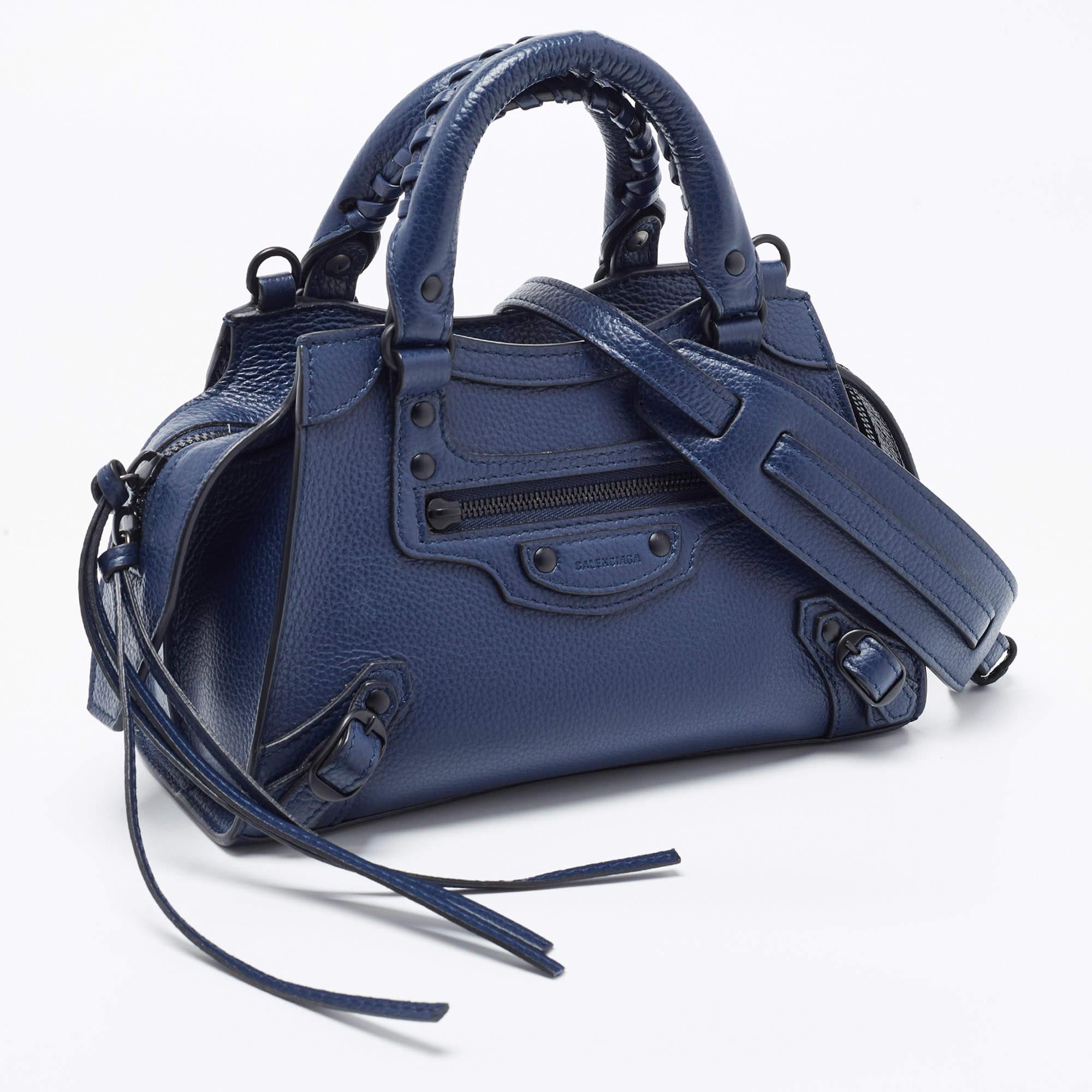 Le fourre-tout City de Balenciaga est un sac à main compact et élégant, fabriqué en cuir bleu foncé de première qualité. Il présente le design Neo Classic emblématique avec des accessoires de couleur noire, une fermeture à glissière sur le dessus et