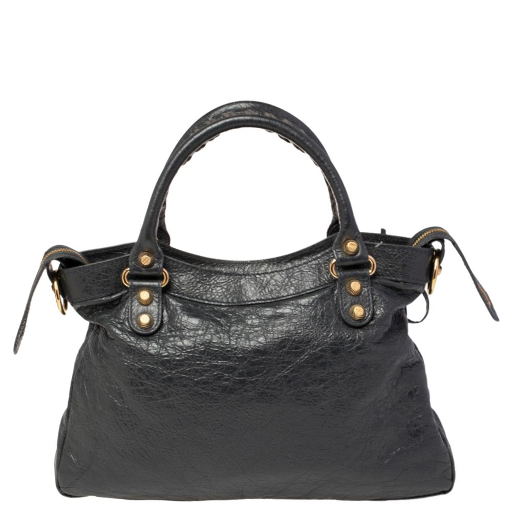 This Balenciaga RH tote is a classic! Crafted from quality leather in a gorgeous dark grey color, the bag has a feminine silhouette with two top handles and gold-tone hardware. The zipper closure opens to a fabric-lined interior and the bag is