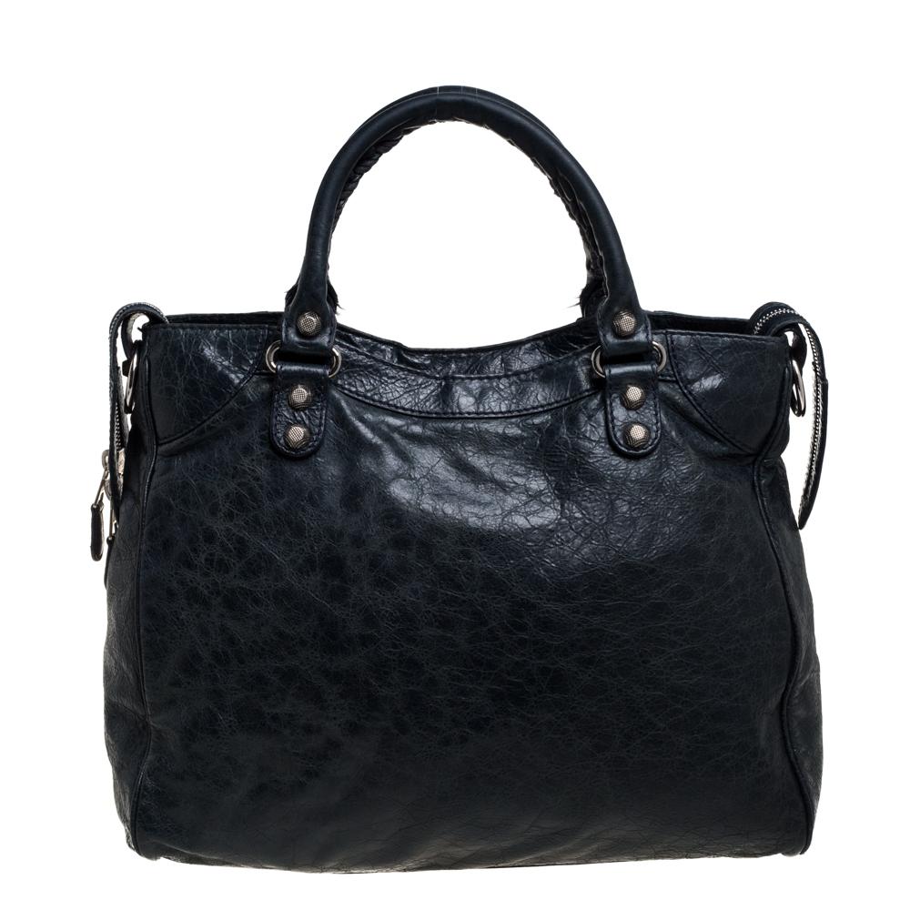 This Balenciaga Velo tote will never leave you unnoticed. The lovely green leather exterior is detailed with silver-tone studs and buckle motifs, a front zip pocket, and double handles. It also has a detachable shoulder strap. It features top zip