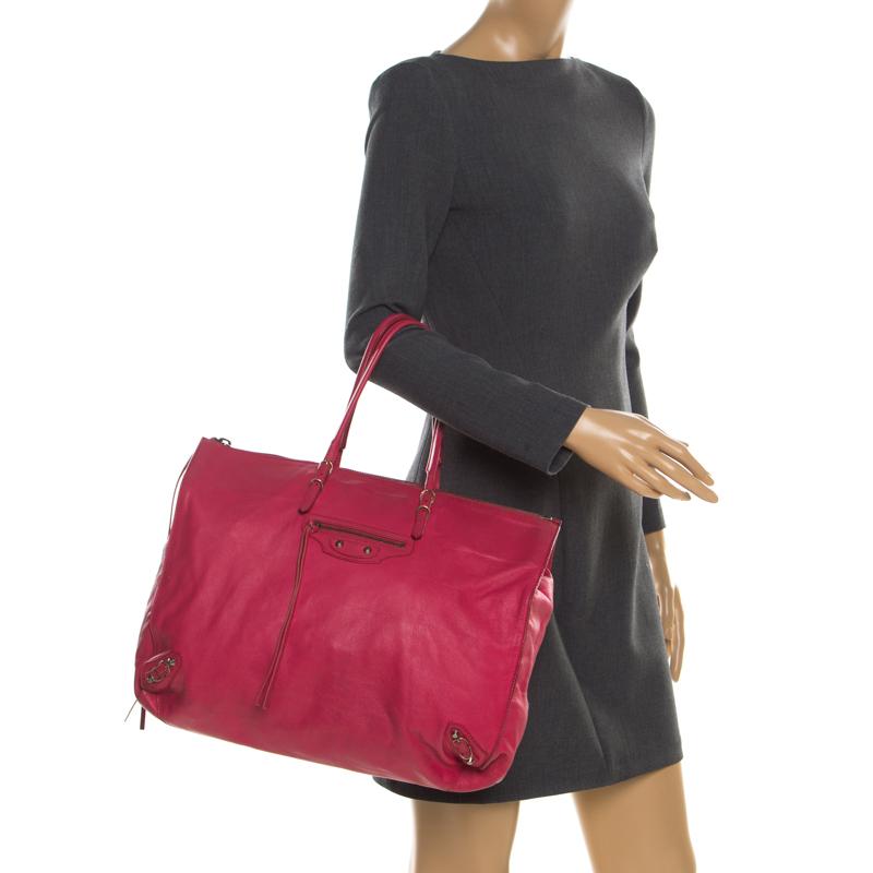This contemporary Balenciaga Papier A4 tote can be perfectly worn as both a weekend or traveling bag. Made from supple dark pink leather, the exterior is detailed with double thin handles, a front zipper pocket, gold-tone buckles, and studs. The